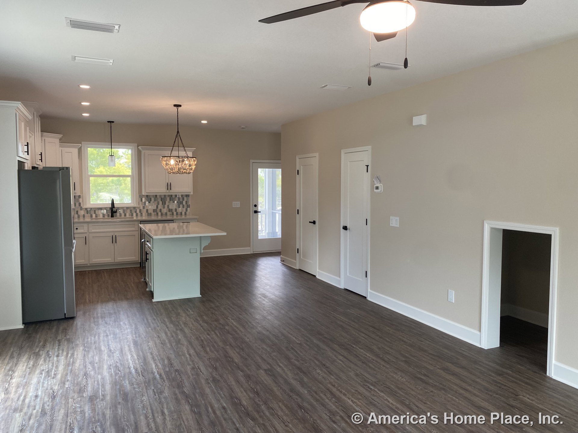 Open kitchen and living area with white shaker cabinets, tile backsplash, central kitchen island, wood-look vinyl flooring, ceiling fan with light, recessed lighting, built-in pet