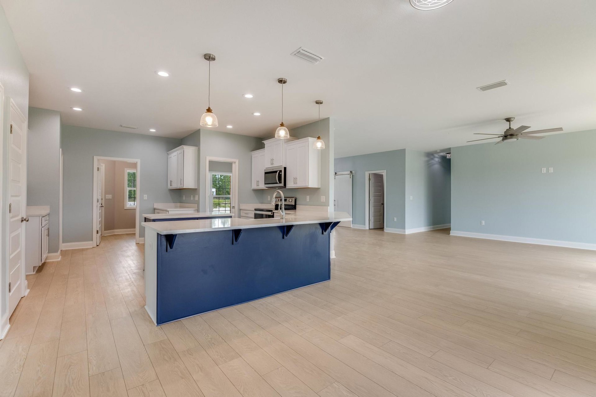 Open kitchen and living room featuring white cabinetry, blue kitchen island countertop, built-in microwave oven, white walls with black trim, white door with black handle, wood