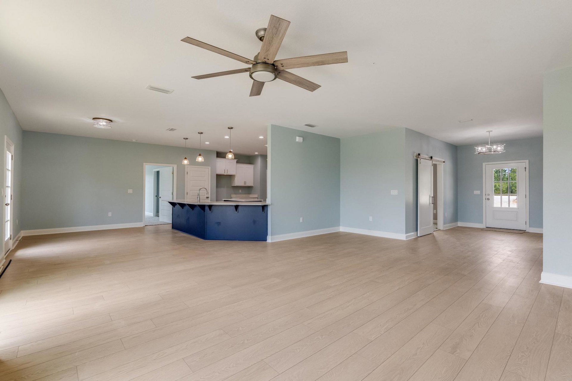 Open-concept kitchen and dining area with wood flooring, blue and white cabinetry, ceiling fan with light, white doors featuring glass panes and silver handles