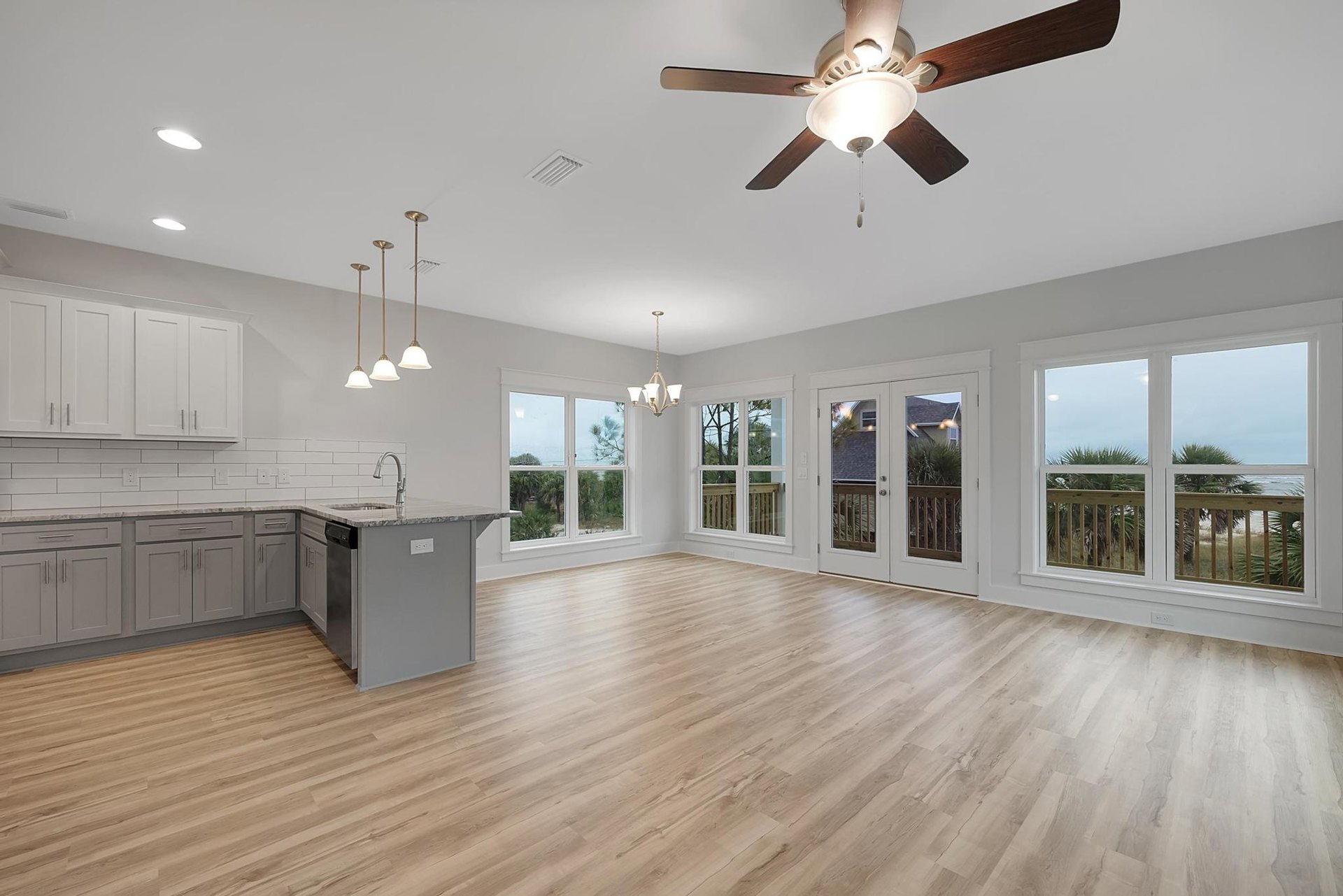 Open kitchen with wood flooring, white cabinetry, central island featuring a built-in sink, ceiling fan with light fixture, recessed ceiling vent, and large windows providing