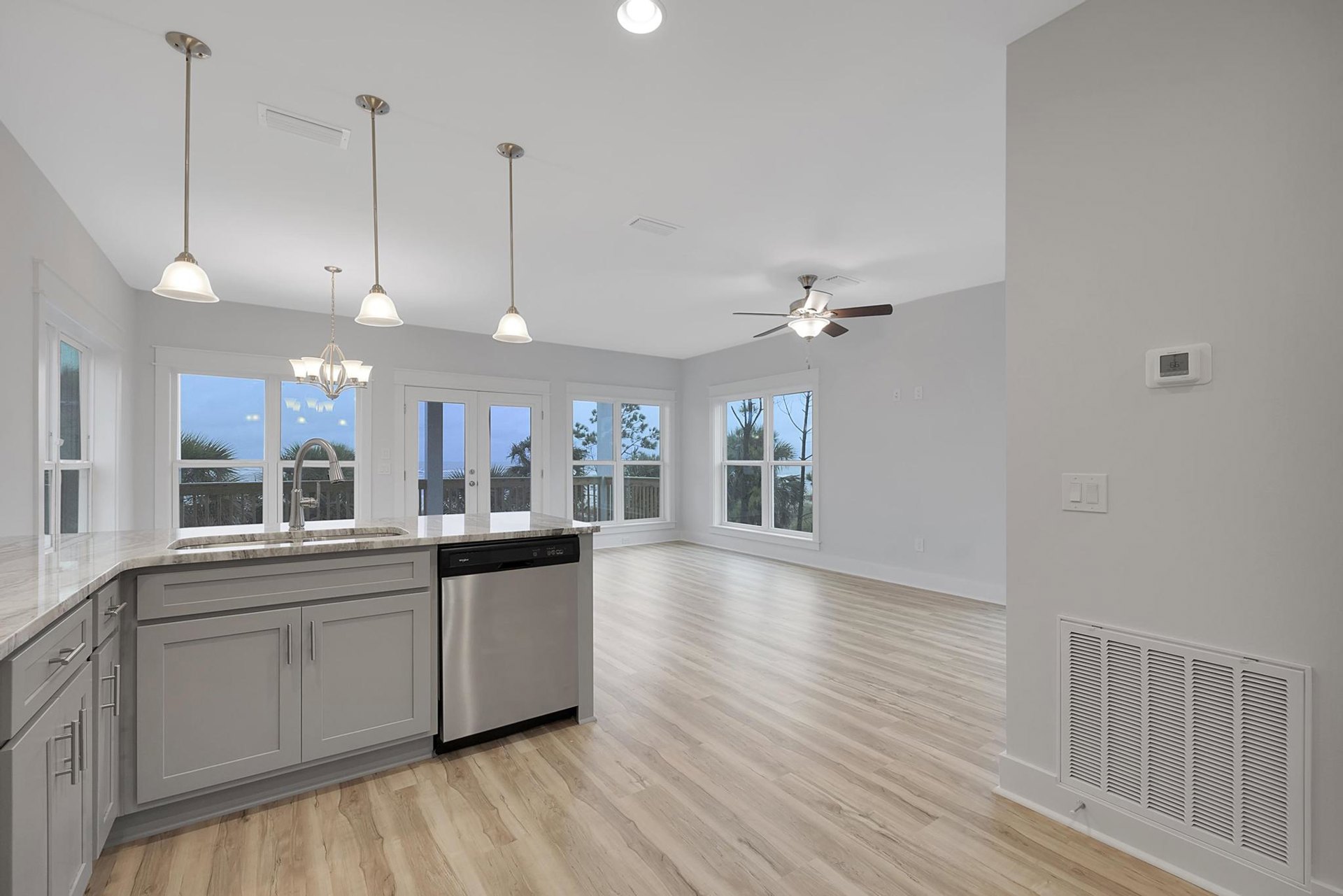 Open kitchen and living room featuring wood flooring, white cabinetry, stainless steel dishwasher with black handle, stone countertops, ceiling fan with light, digital thermostat