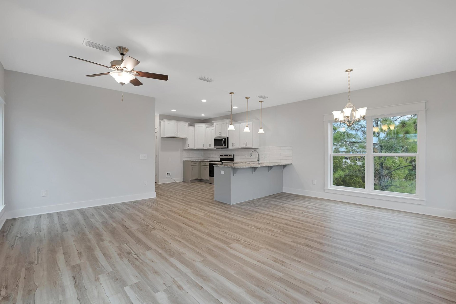 Open-concept kitchen with marble island, open microwave, hardwood floors, white walls, ceiling fan with light, window showing trees outside