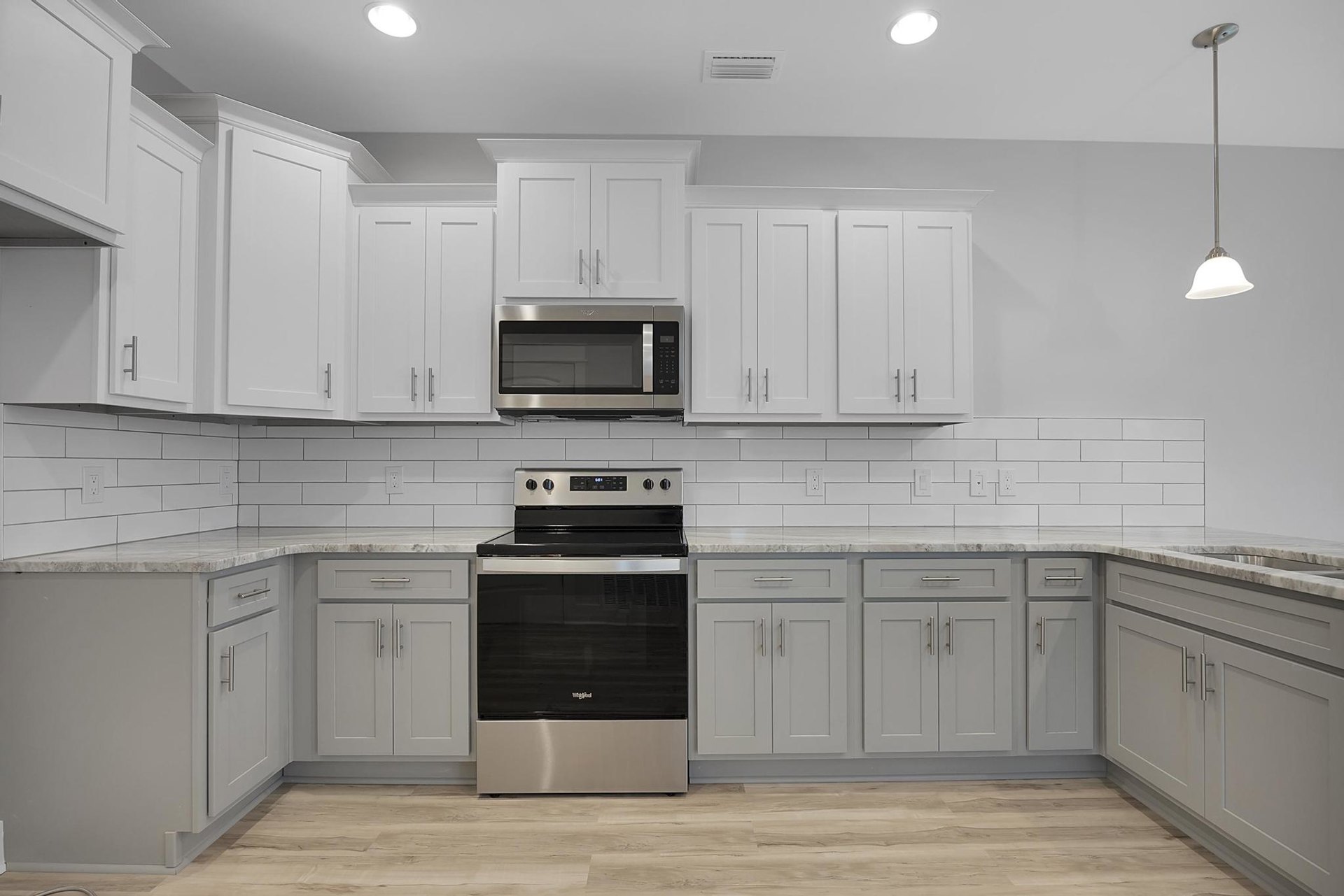 White shaker cabinets, black and stainless steel stove, black microwave with silver handle, wood flooring, light quartz countertops, upper and lower cabinetry
