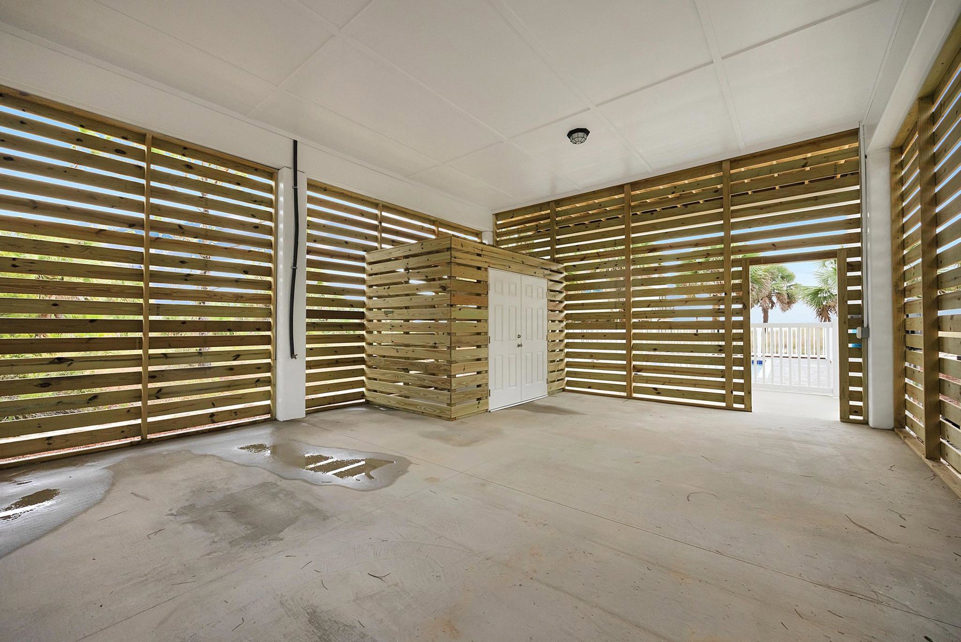 Wooden walls with visible structural beams, white door, window with blinds, concrete floor, wooden crate, and white ceiling with linear detailing.