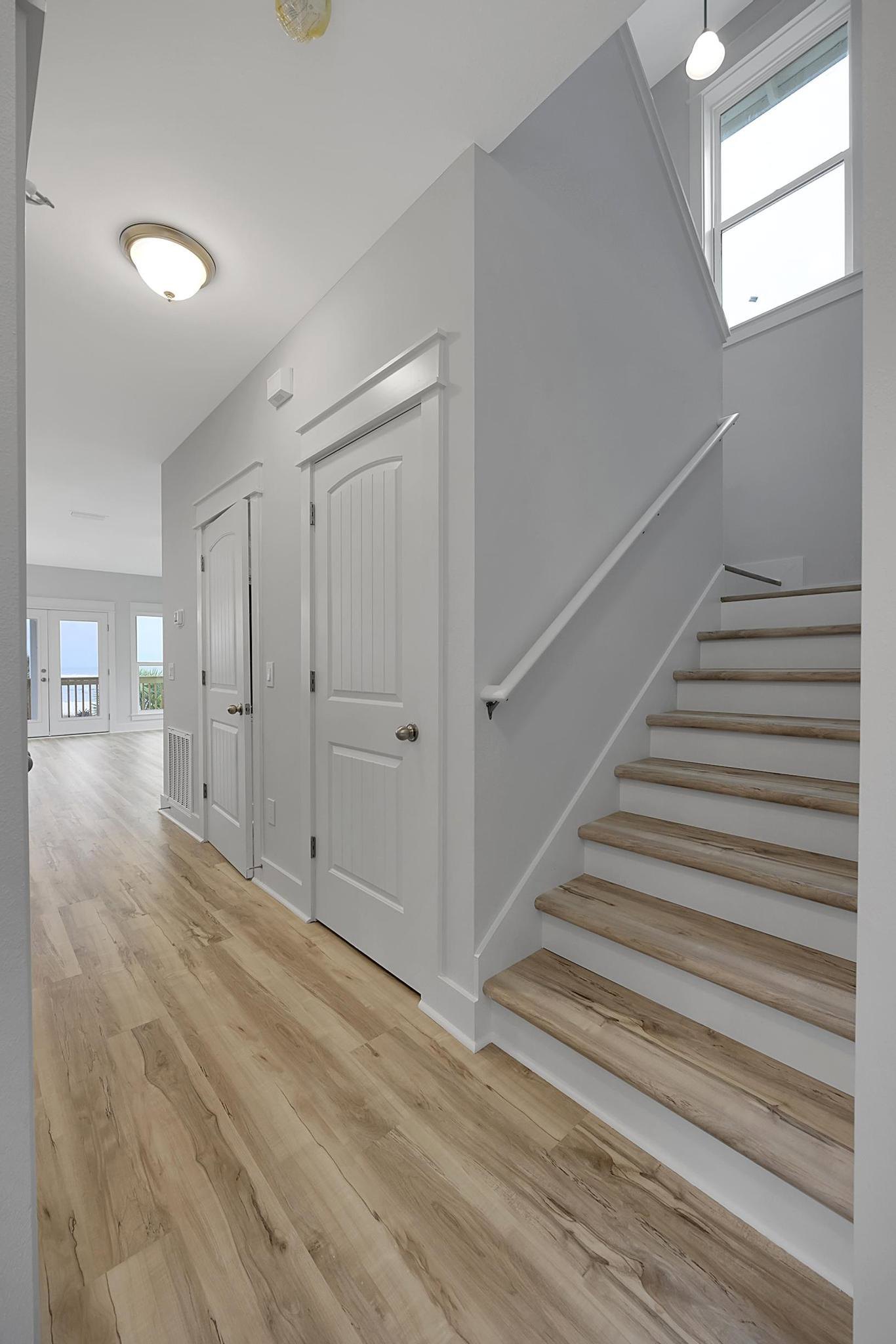 Hallway with wood flooring, white plaster walls, staircase with wood handrail, white doors, ceiling light fixture, and window with white frame