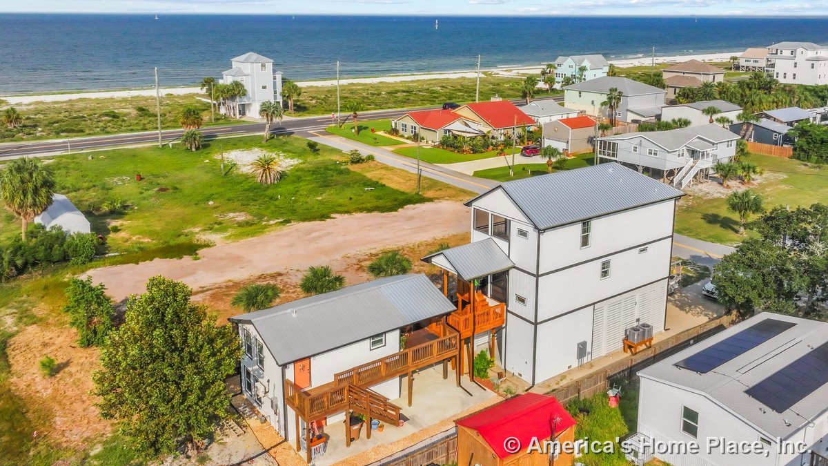 Coastal multi-story home with metal roof, elevated wooden decks, exterior staircases, covered porch, large windows, siding, garage door, and ocean view.