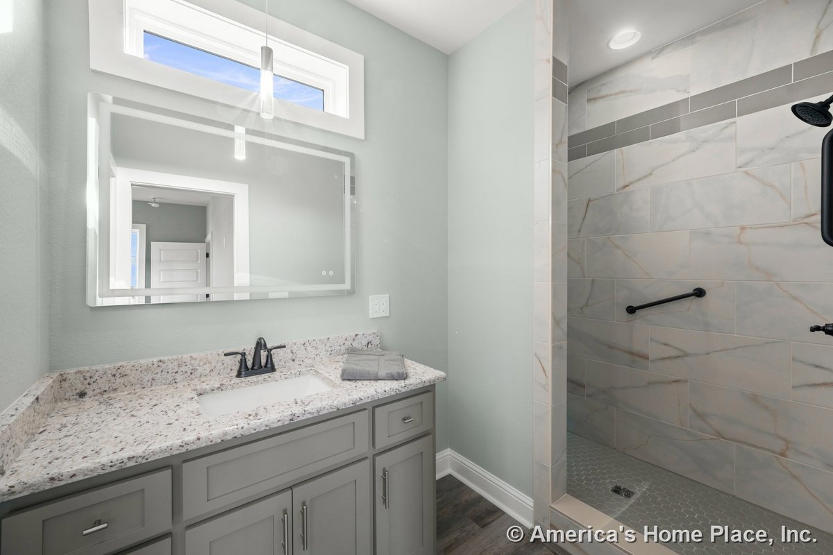 Walk-in shower with large marble-look tile, quartz vanity countertop, gray shaker cabinetry, single undermount sink, frameless wall mirror, modern pendant light, transom window