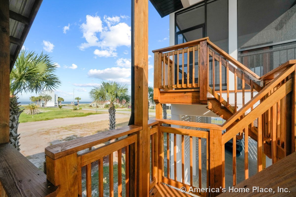 Multi-level wooden staircase with vertical wood railings leads to an elevated porch and covered entry area, showcasing coastal exterior design and natural wood finishes.
