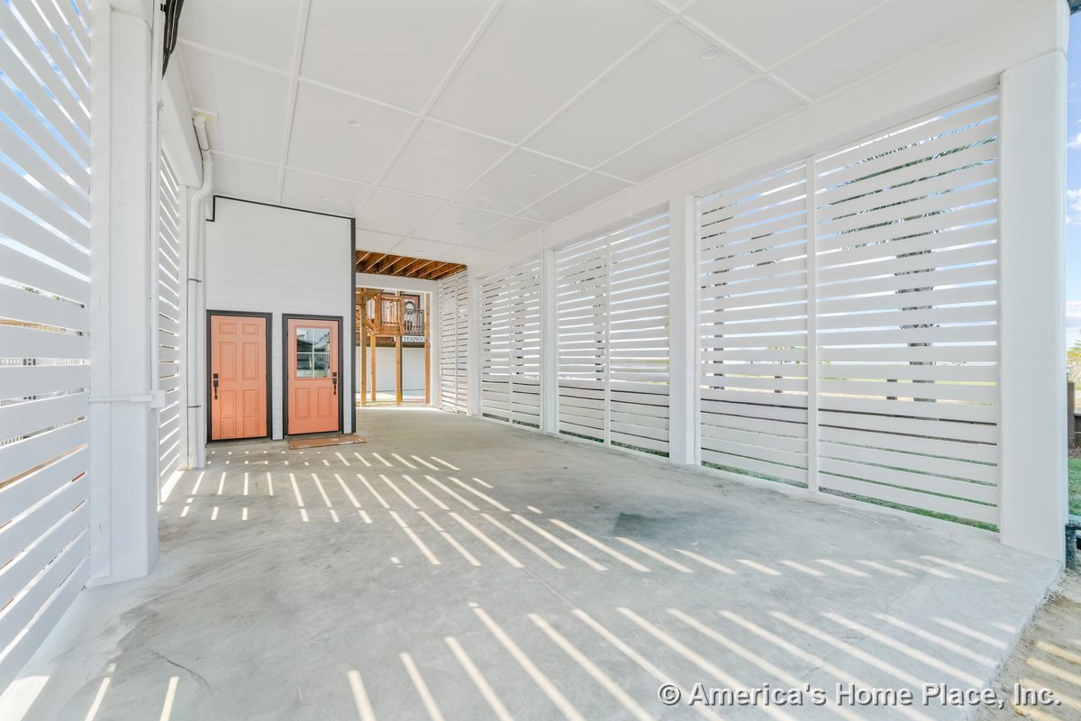 Covered exterior entry area with slatted white privacy walls, concrete flooring, two orange doors with black trim, white paneled ceiling, and built-in lighting fixtures.