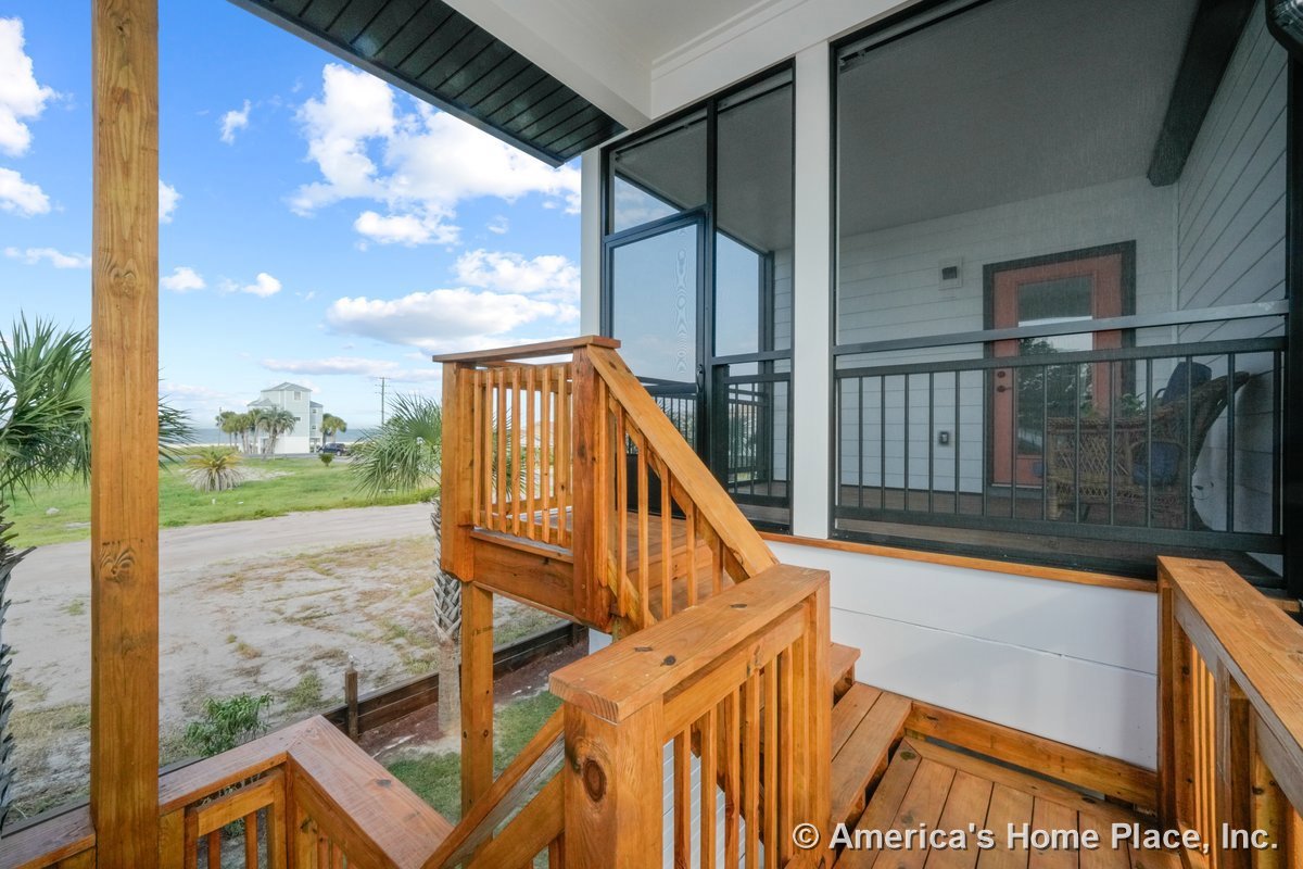 Wooden exterior staircase with black railing leads to a screened porch featuring large glass windows, glass entry door, and white siding exterior with contrasting trim.