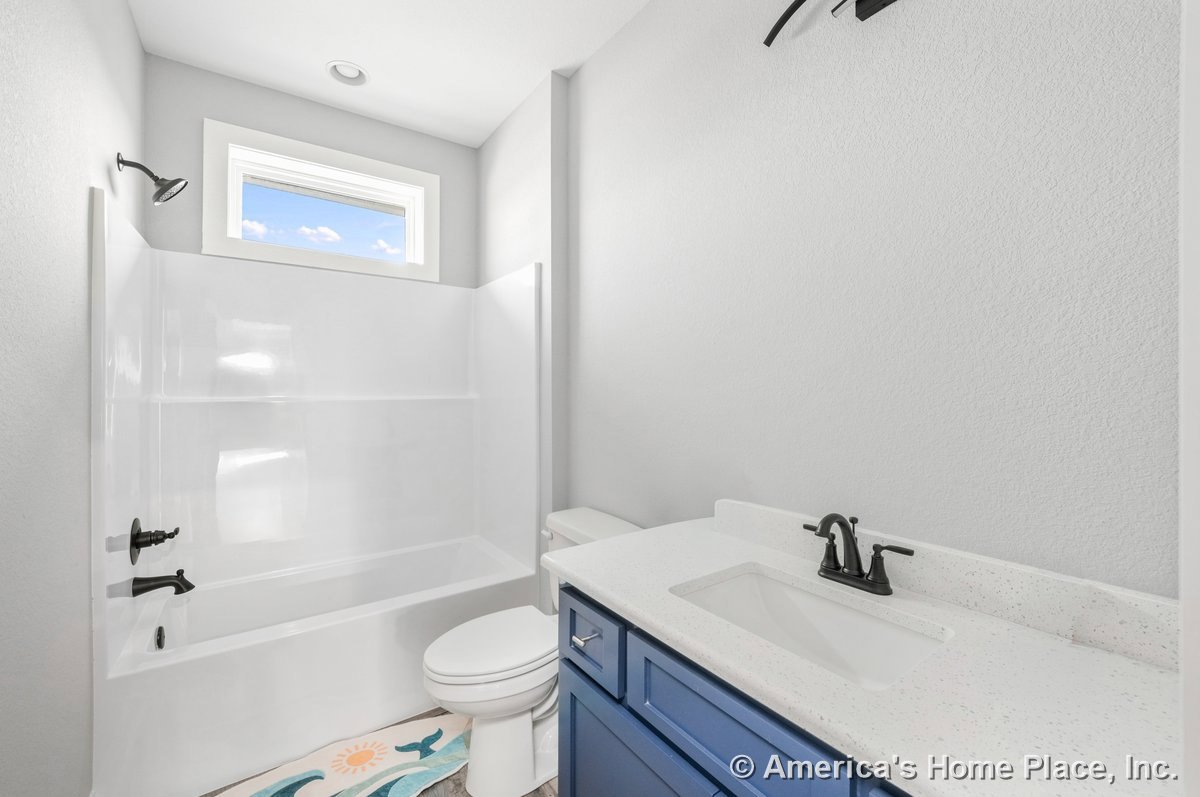 White bathtub with integrated shower and matte black fixtures, blue vanity cabinetry topped with quartz countertop and undermount sink, rectangular window with trim above tub