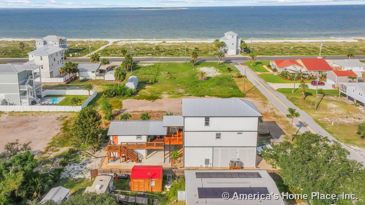 Coastal multi-story home with metal roof, elevated foundation, multiple exterior staircases, covered porch, large windows, and wood railings.