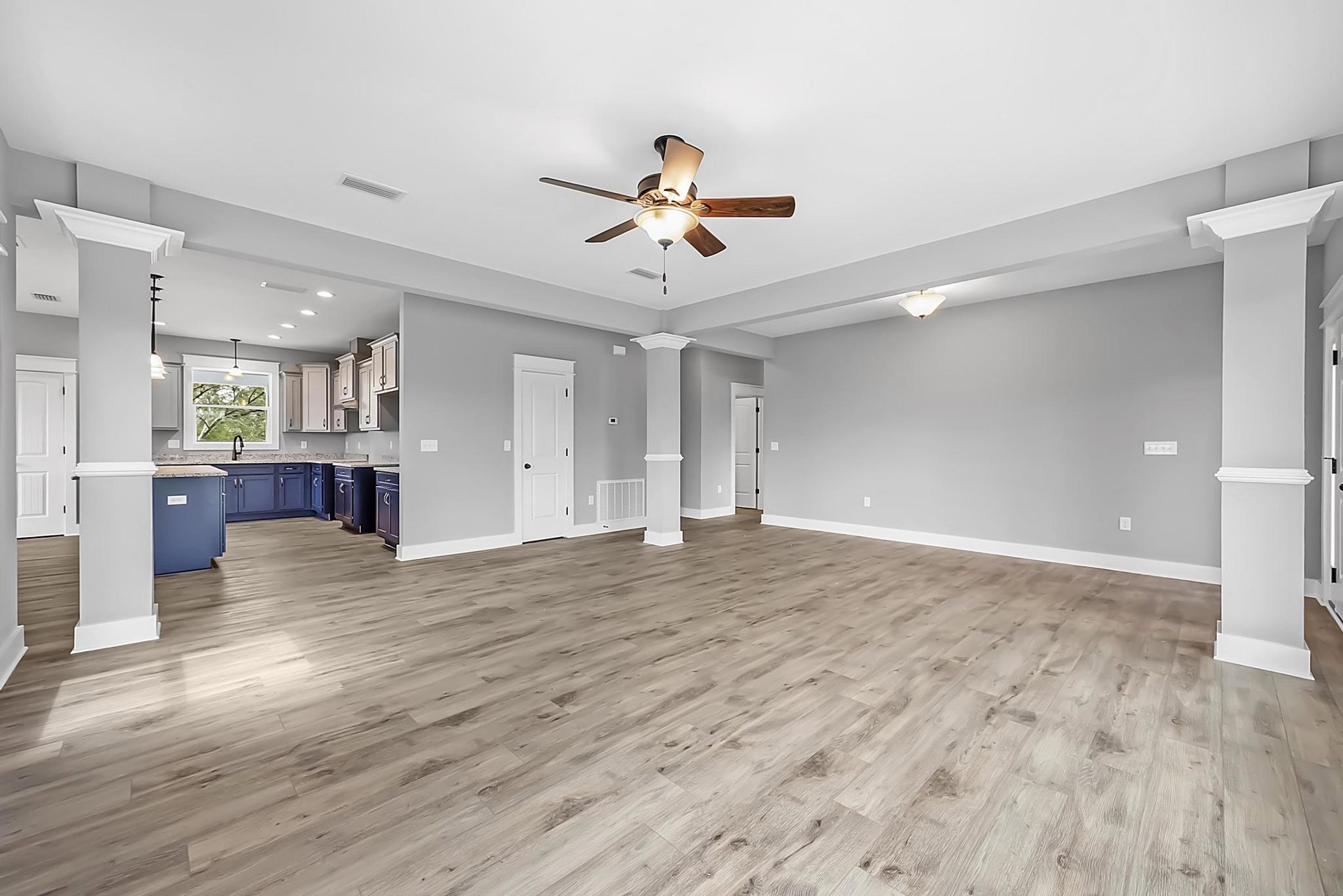 Spacious room featuring wood flooring, white paneled walls, ceiling fan with light, white door with black knobs, window with white frame, and white sink.