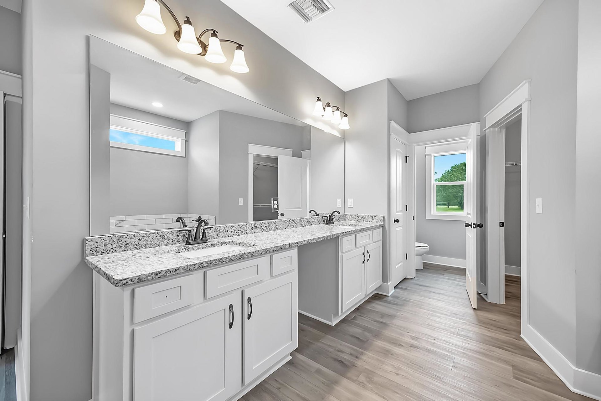 Bathroom with marble countertop, white cabinetry, chrome faucet, tile backsplash, window with white frame, wood flooring, ceiling vent, and recessed lighting.