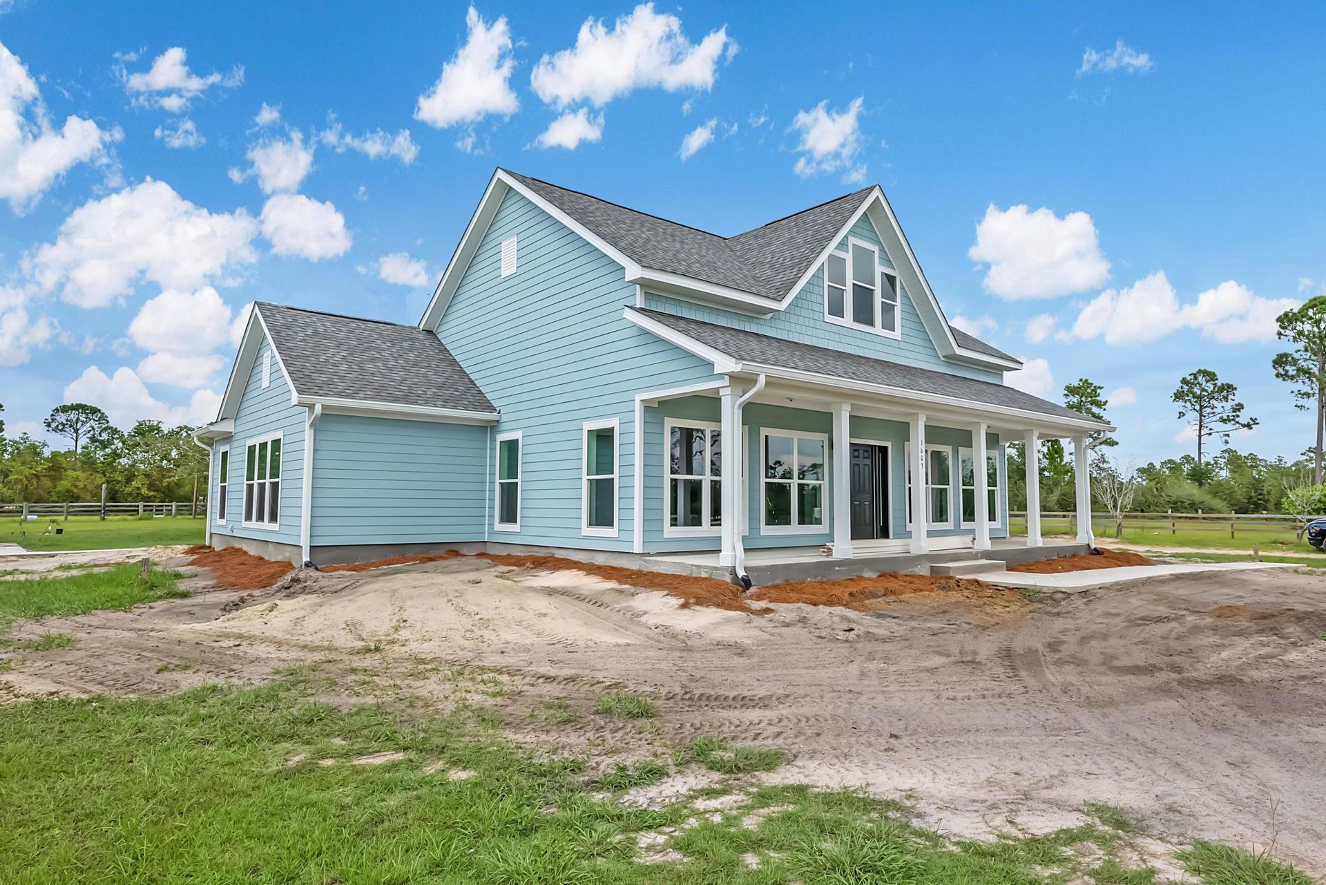 Blue house with white trim and blue roof, black door with white frame, window with white frame, dirt hill and patch in front, trees and Robert Frost Farm visible in background