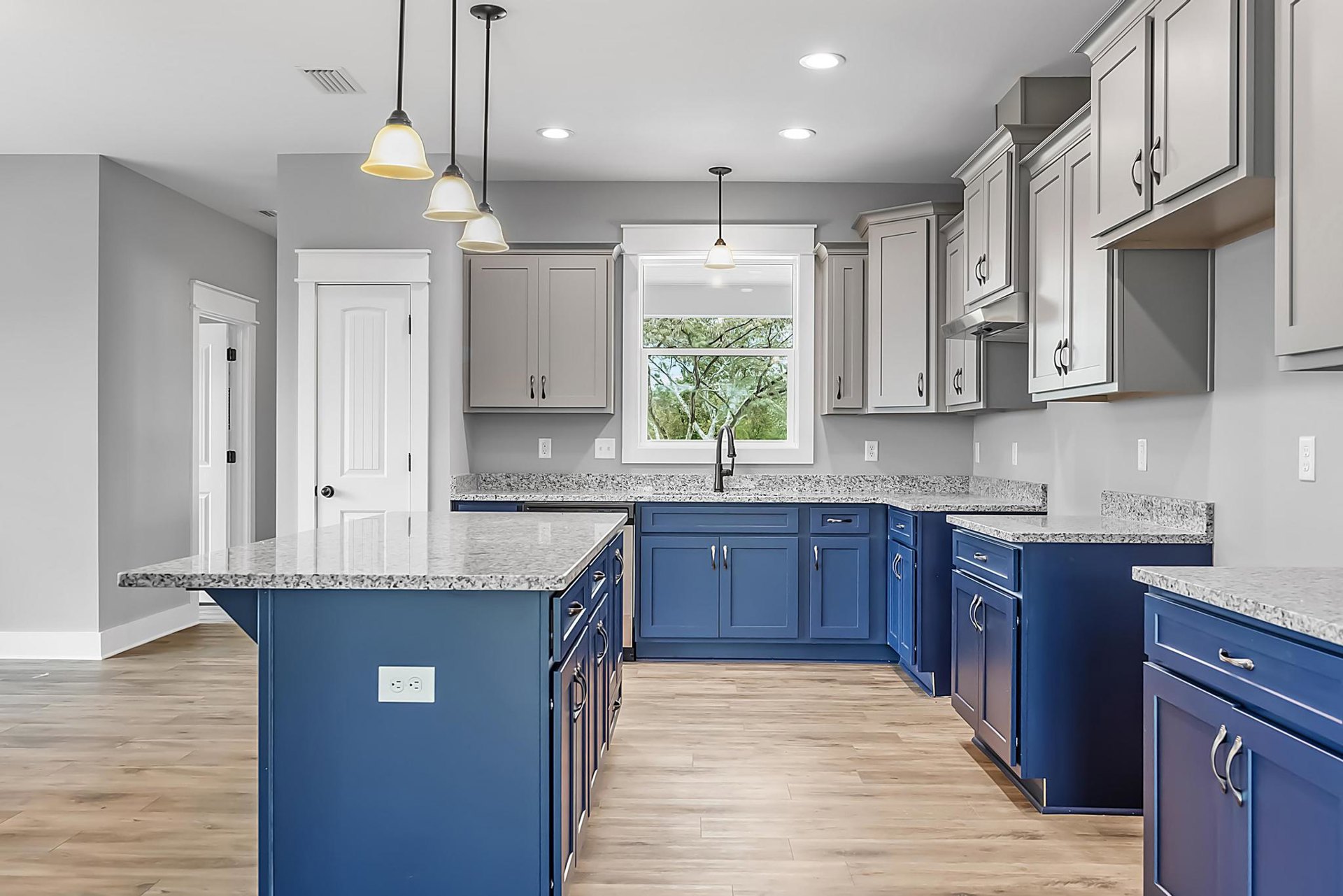 Blue shaker cabinets with brushed nickel hardware, white quartz countertops, stainless steel sink, kitchen island with granite surface, light wood flooring, and modern appliances.
