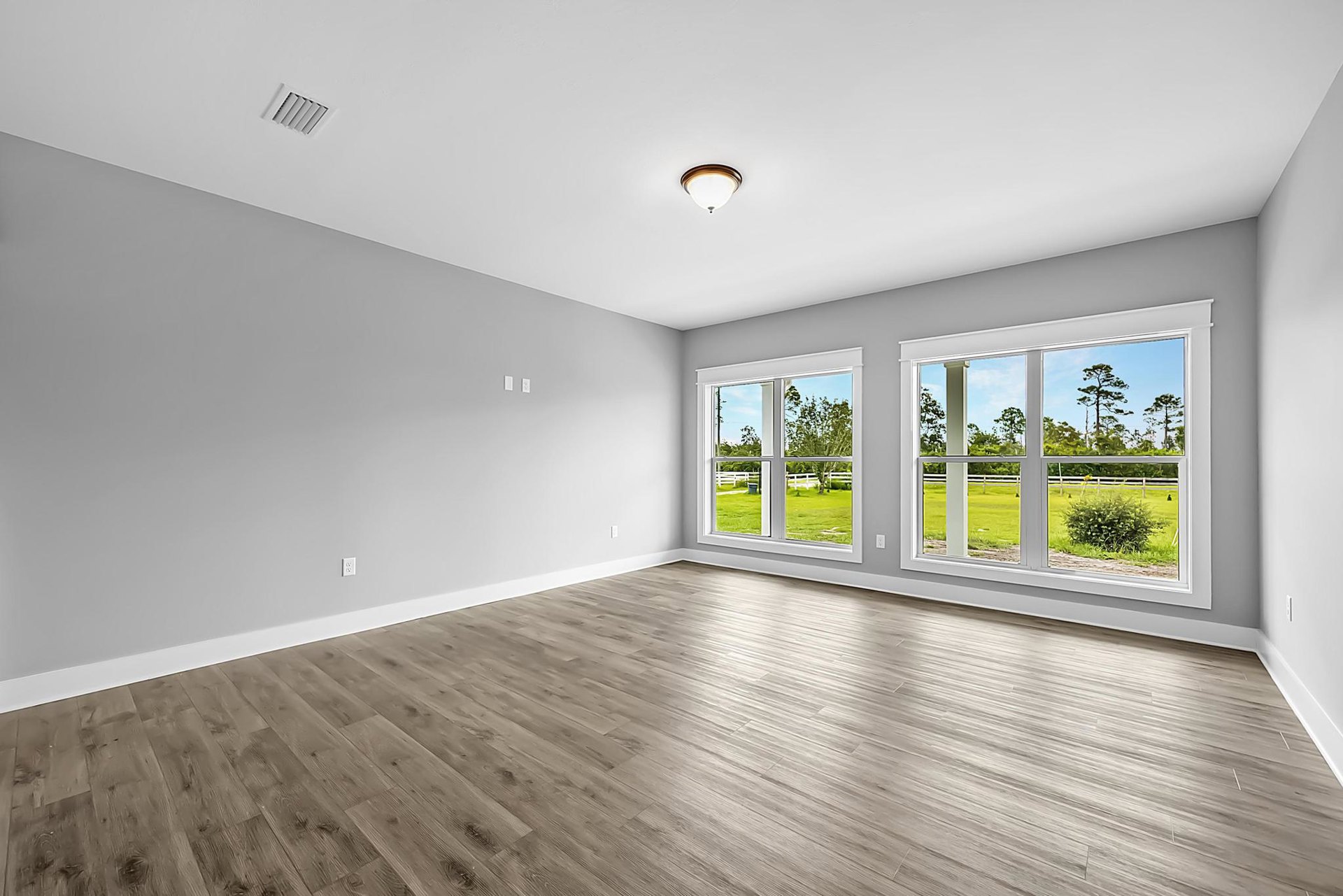 Spacious room featuring large windows, light wood flooring, white plaster walls, and recessed ceiling vent