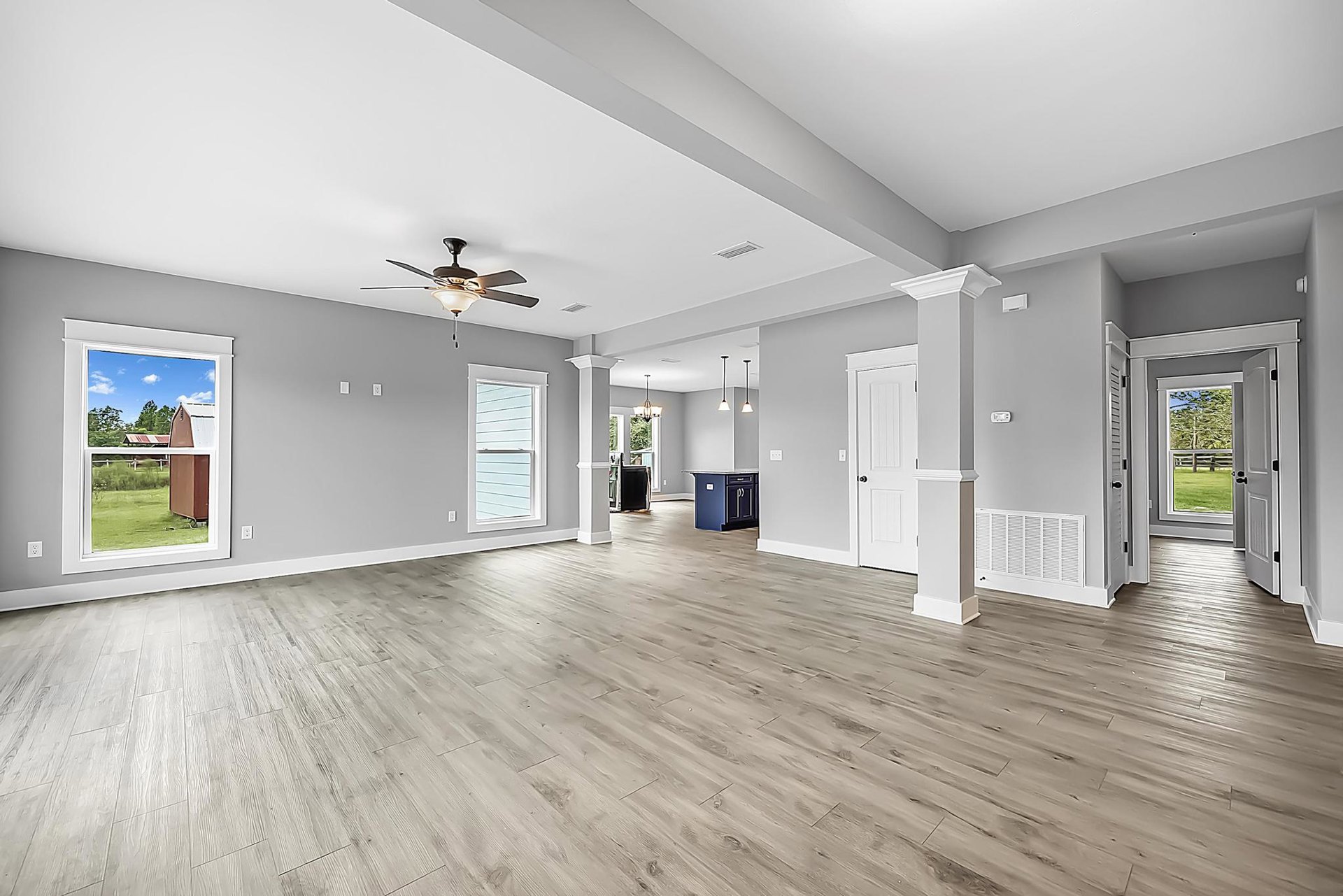 Spacious room with wood flooring, ceiling fan with light fixture, blue and black cabinet, large window overlooking barn and shed