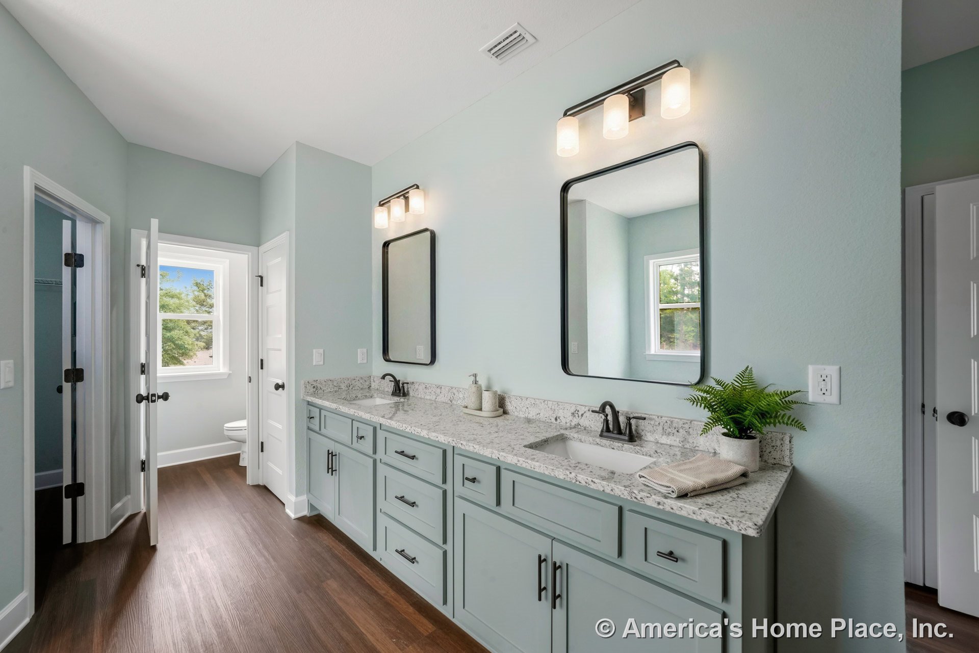 Double vanity with granite countertop and shaker-style cabinets, dual sinks, wall-mounted mirrors, three-light matte black vanity fixtures, wood-look flooring, light blue walls