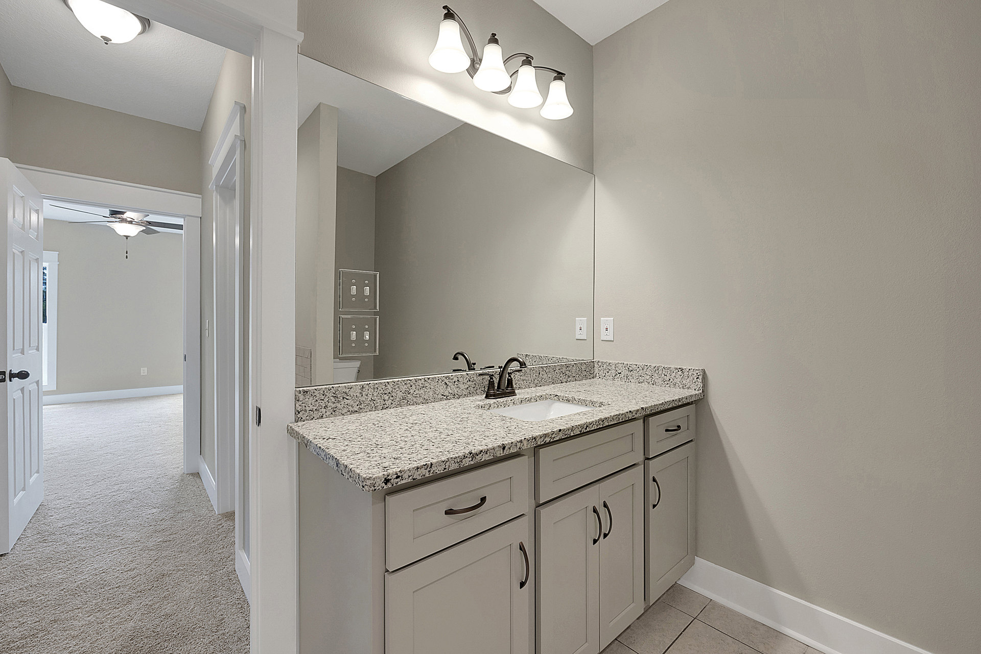 Marble countertop with undermount sink, expansive wall mirror, white cabinetry, chrome faucet, and multi-bulb light fixture in a modern bathroom