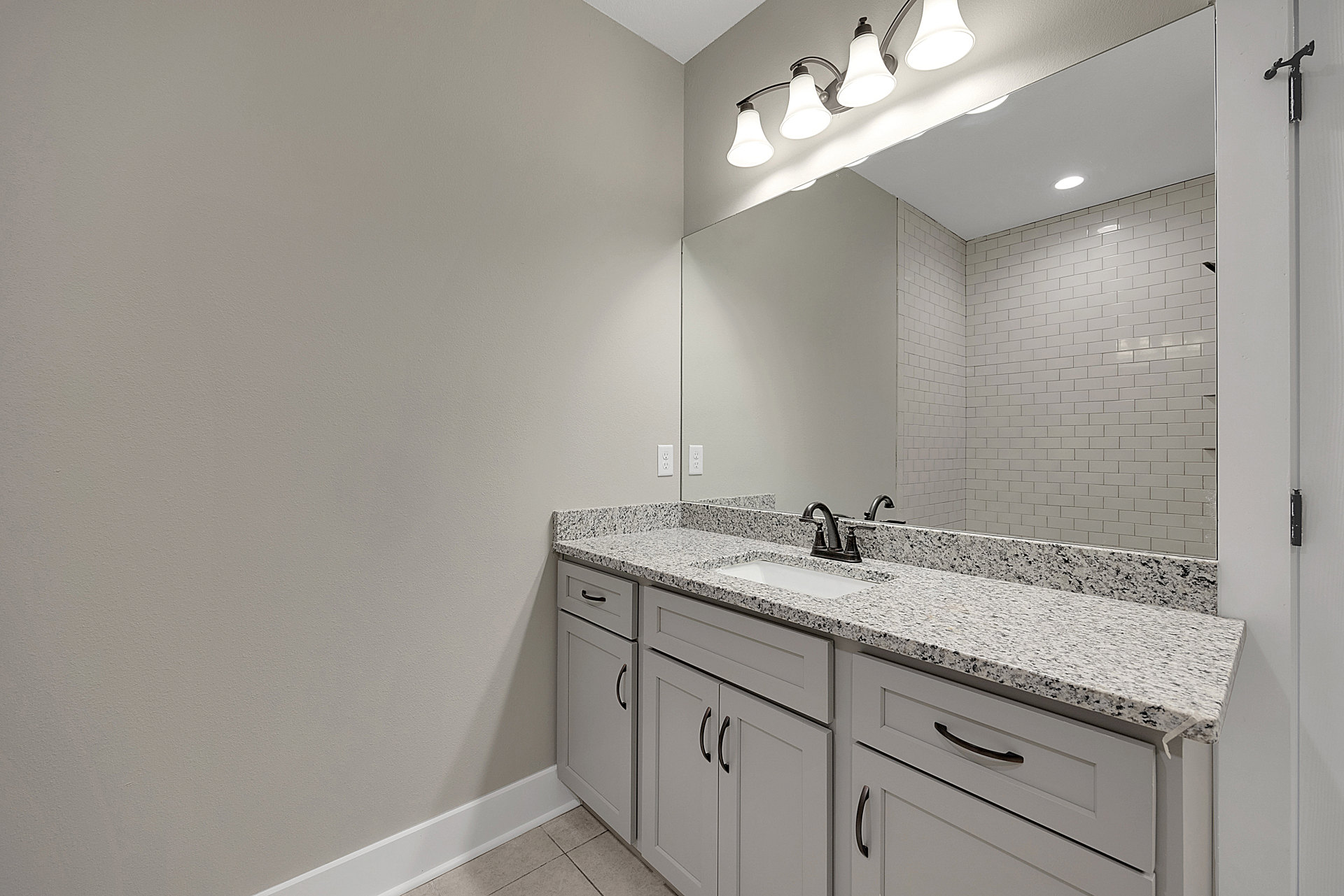 Bathroom with marble countertop, rectangular mirror, white sink, brushed nickel faucet, white cabinetry, and three-light fixture above mirror