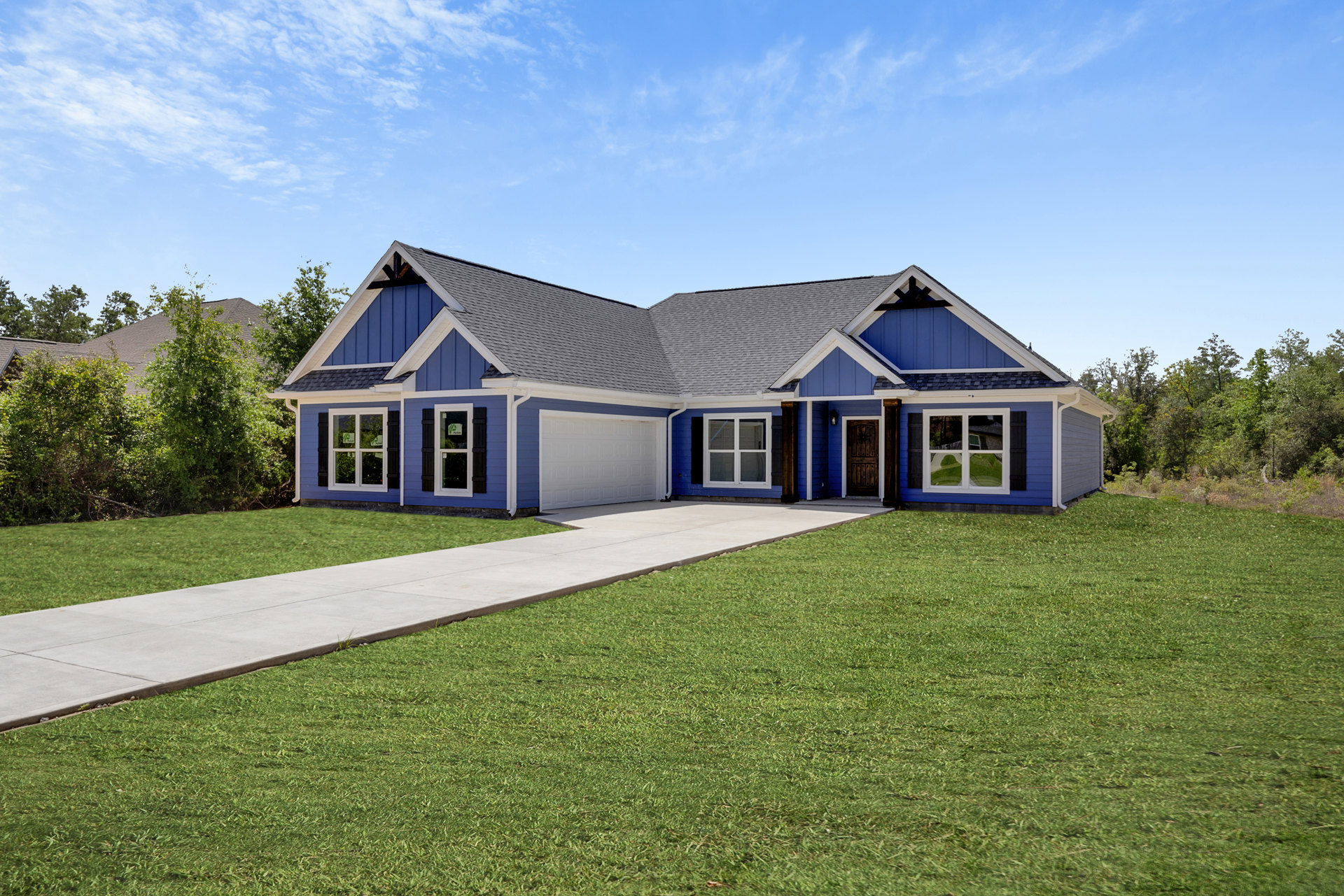 Blue siding house with attached garage, concrete driveway, green lawn, and covered front porch under a partly cloudy sky