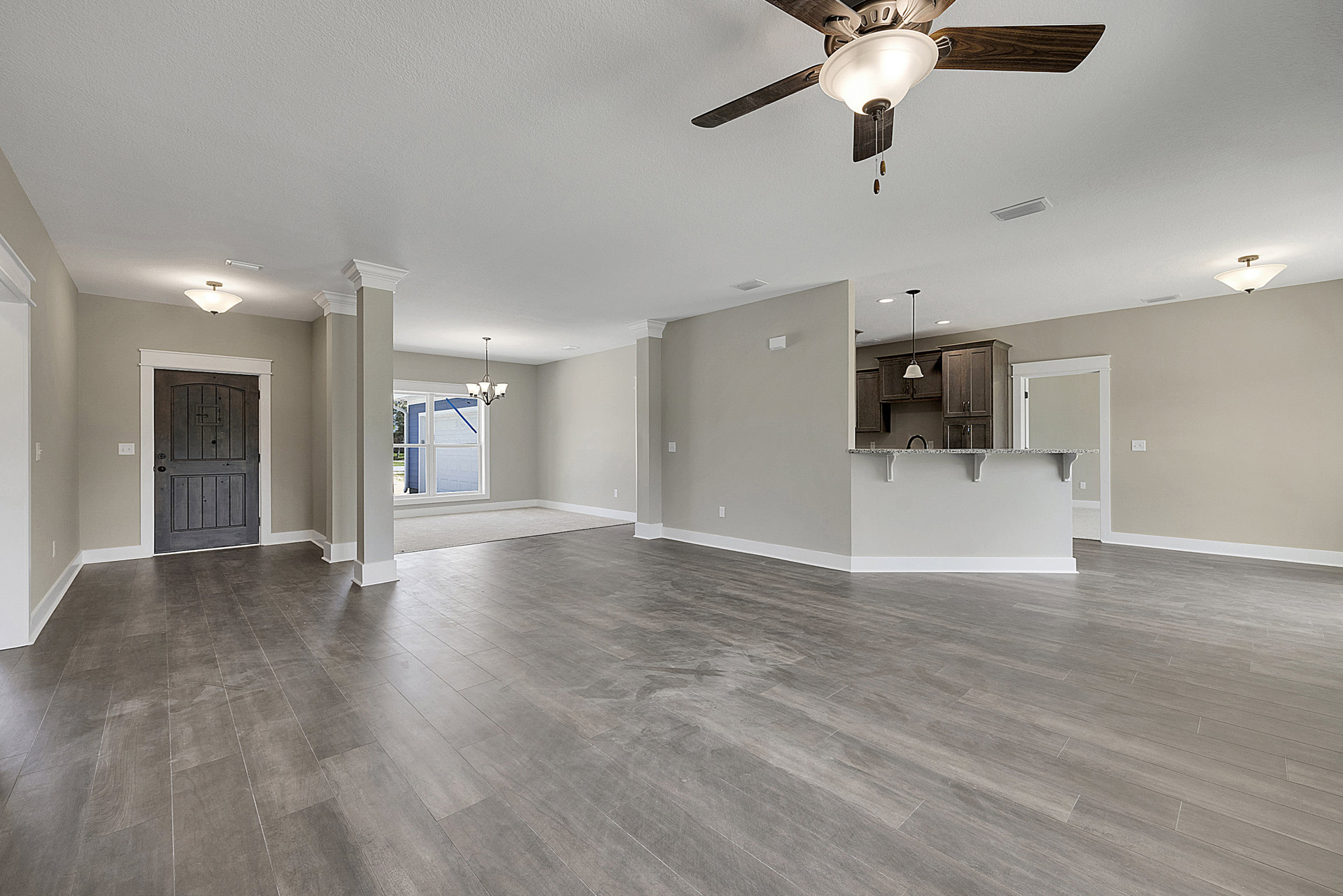 Spacious room featuring grey wood flooring, white walls, ceiling fan with light fixture, blue accent wall with window, and close-up views of a door and light fixture