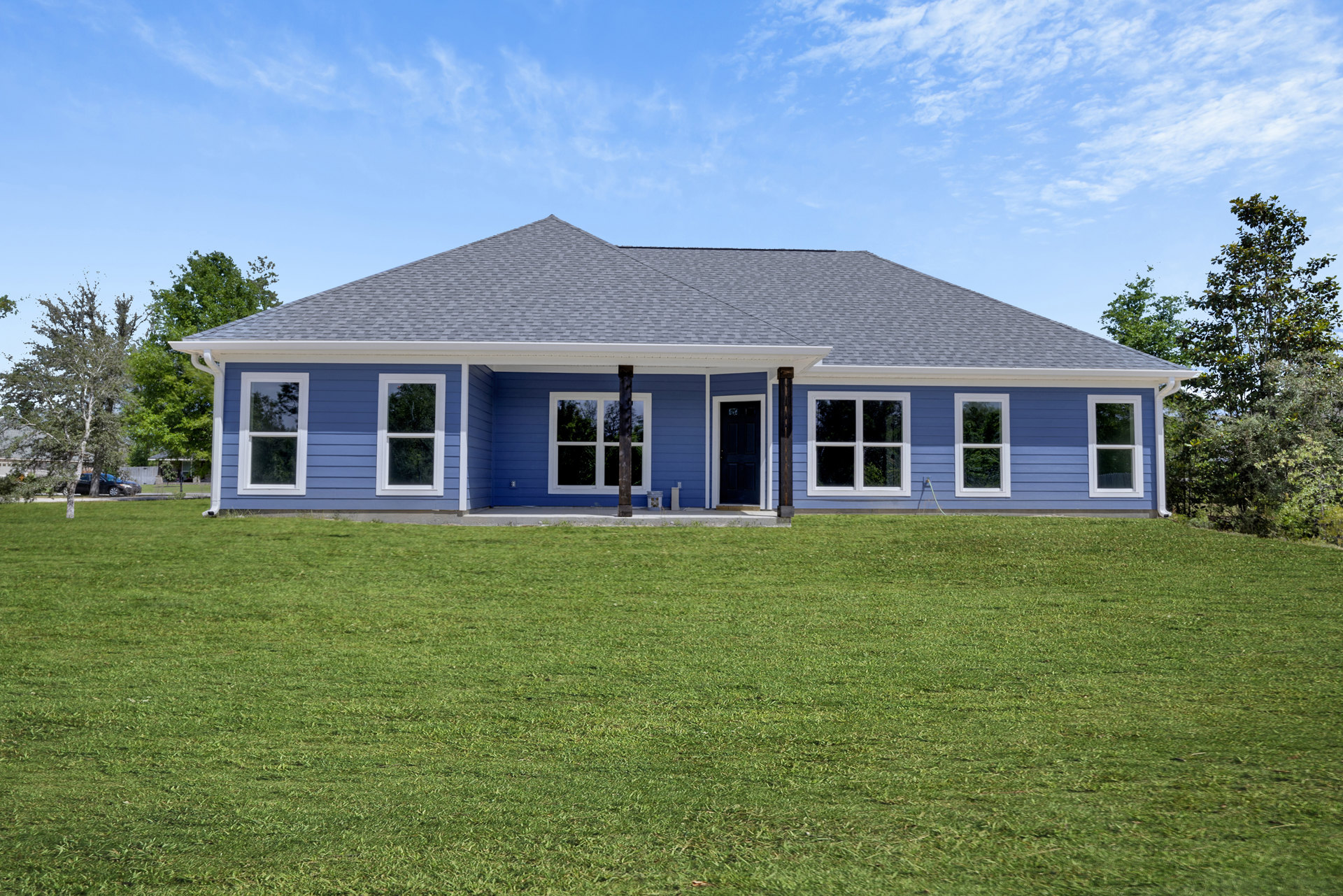 Blue house with white trim and blue door, manicured green lawn, white-framed windows, porch, leafy tree in background, partly cloudy sky.