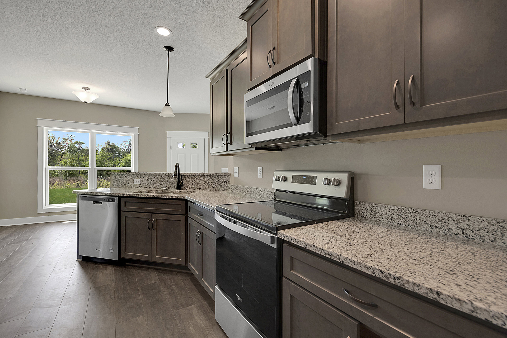Granite countertops, stainless steel stove and oven, white cabinetry, built-in microwave, dishwasher, electrical outlet, kitchen window with view of trees
