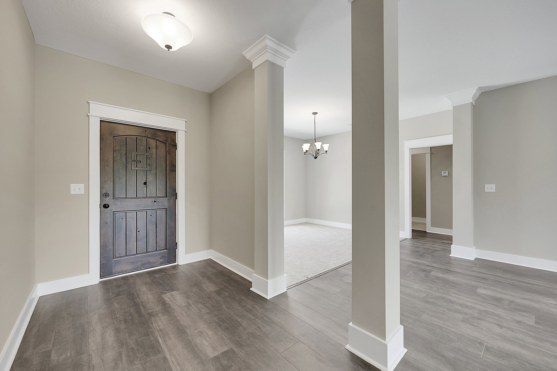 Wood floor room with white plaster walls, wooden door featuring a square window and lock, ceiling-mounted chandelier, and light switch beside the door.