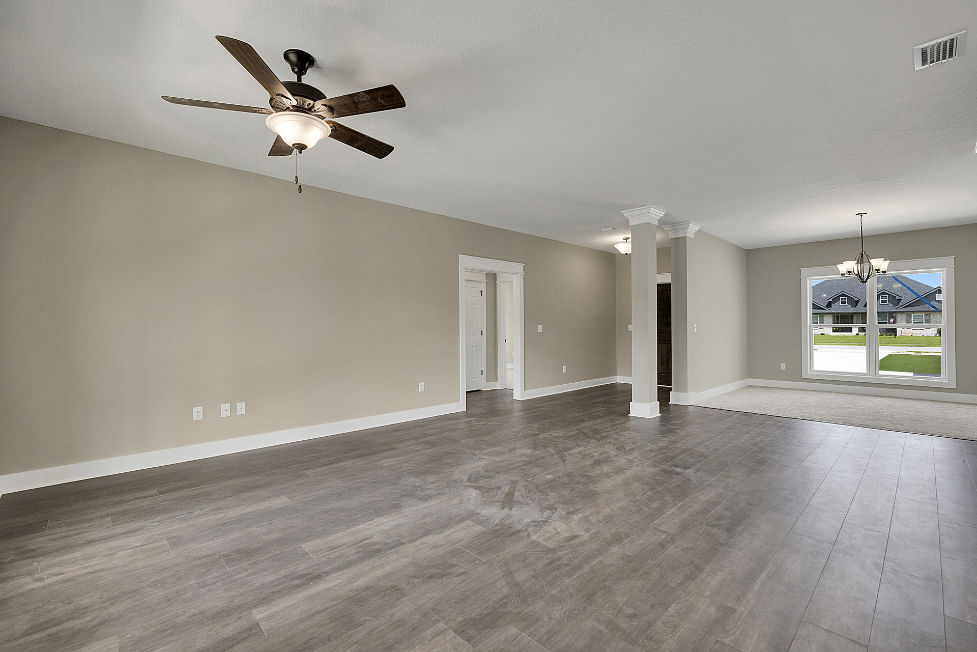 Spacious room with wood flooring, white plaster walls, ceiling fan with light fixture, and window overlooking lawn and neighboring house