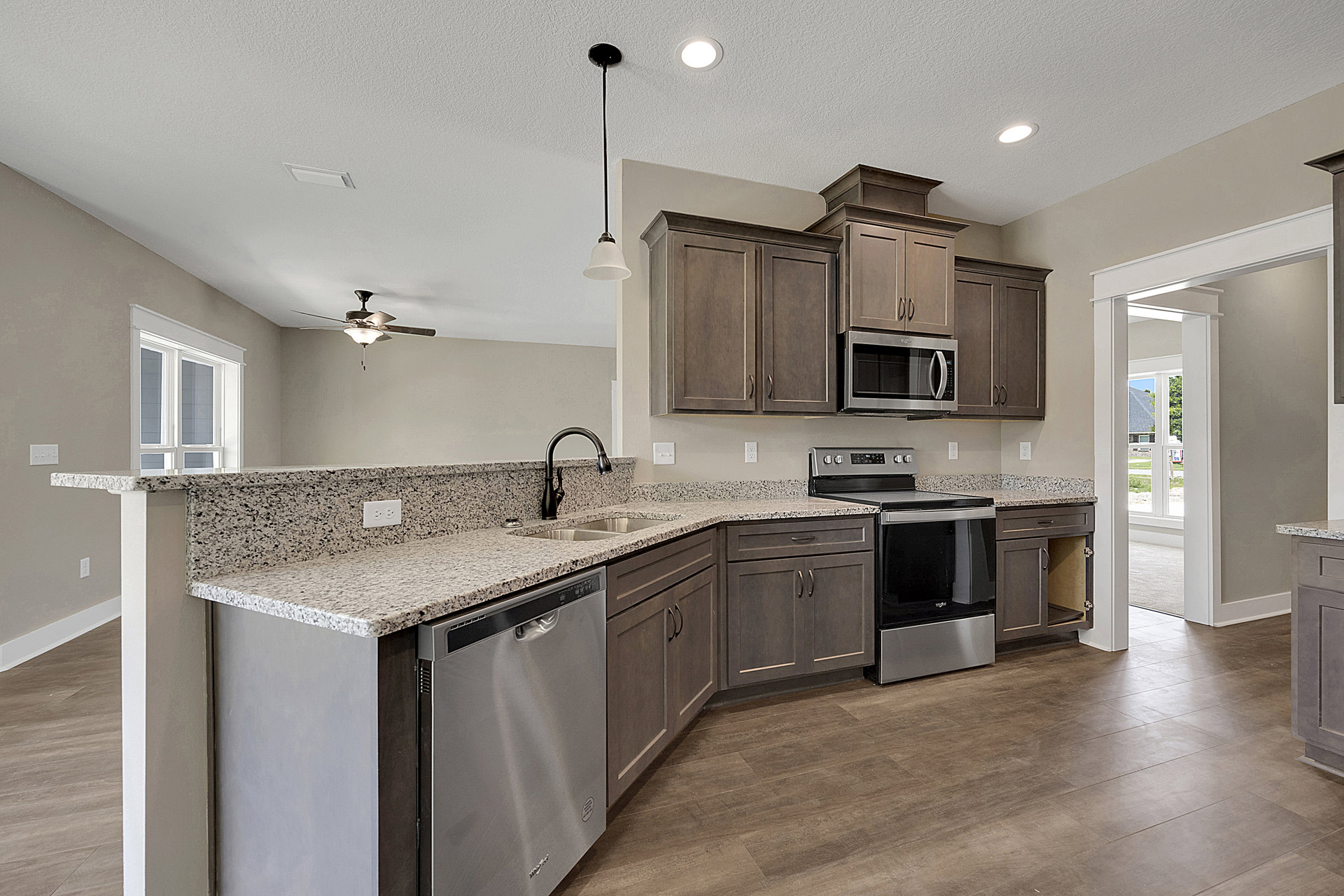 Granite countertops, stainless steel appliances including microwave, stove, oven, and dishwasher, tile backsplash, wood cabinetry, chrome faucet, visible crack in wall near sink