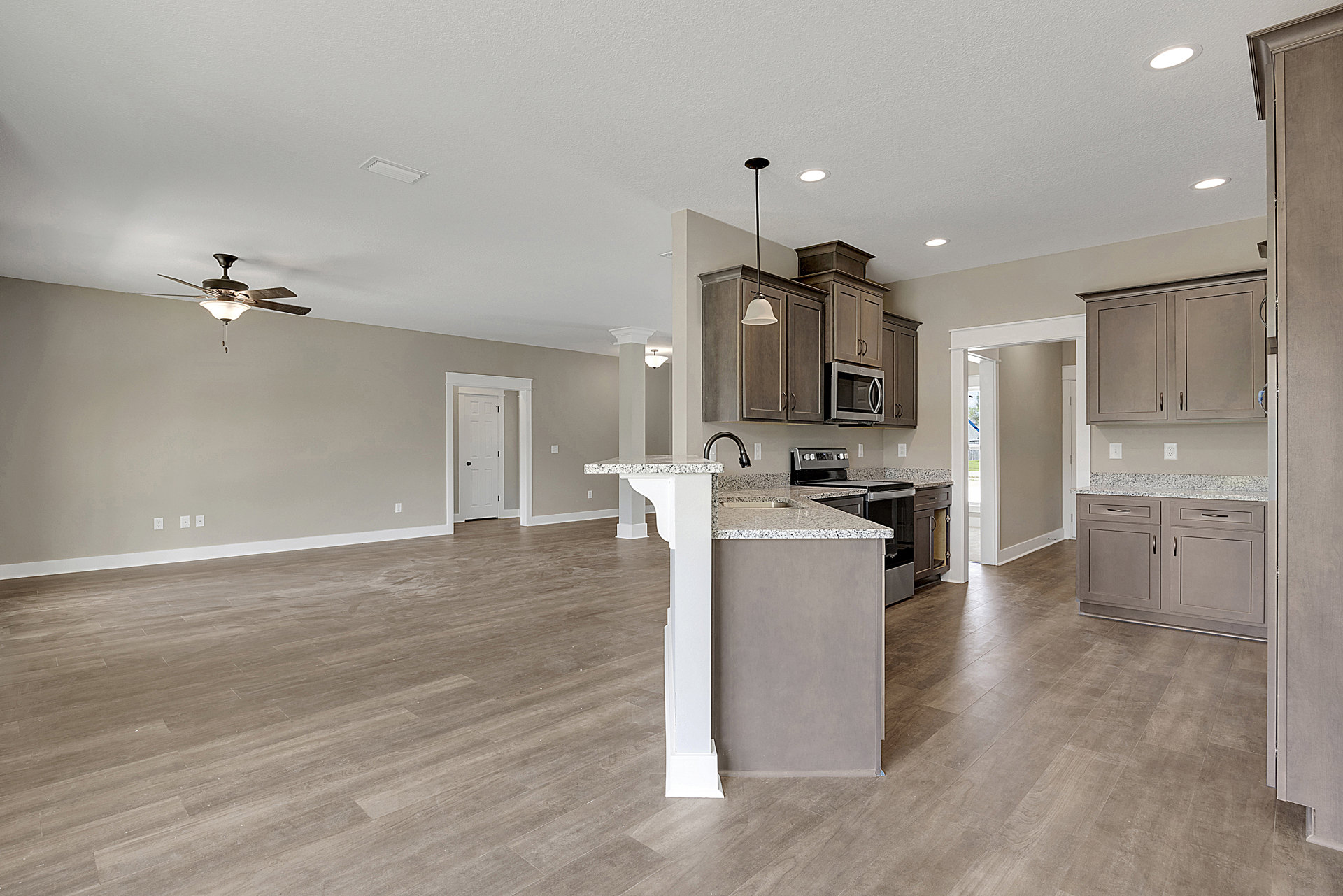 Open-concept kitchen and living room featuring a ceiling fan with light fixture, kitchen island with granite countertops, white cabinetry, stainless steel microwave, and white door