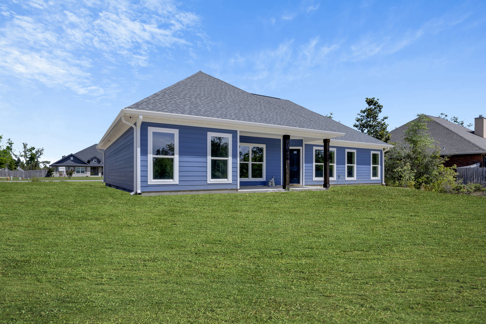 Blue siding house with white trim and blue front door, manicured green lawn, large windows reflecting trees and sky.