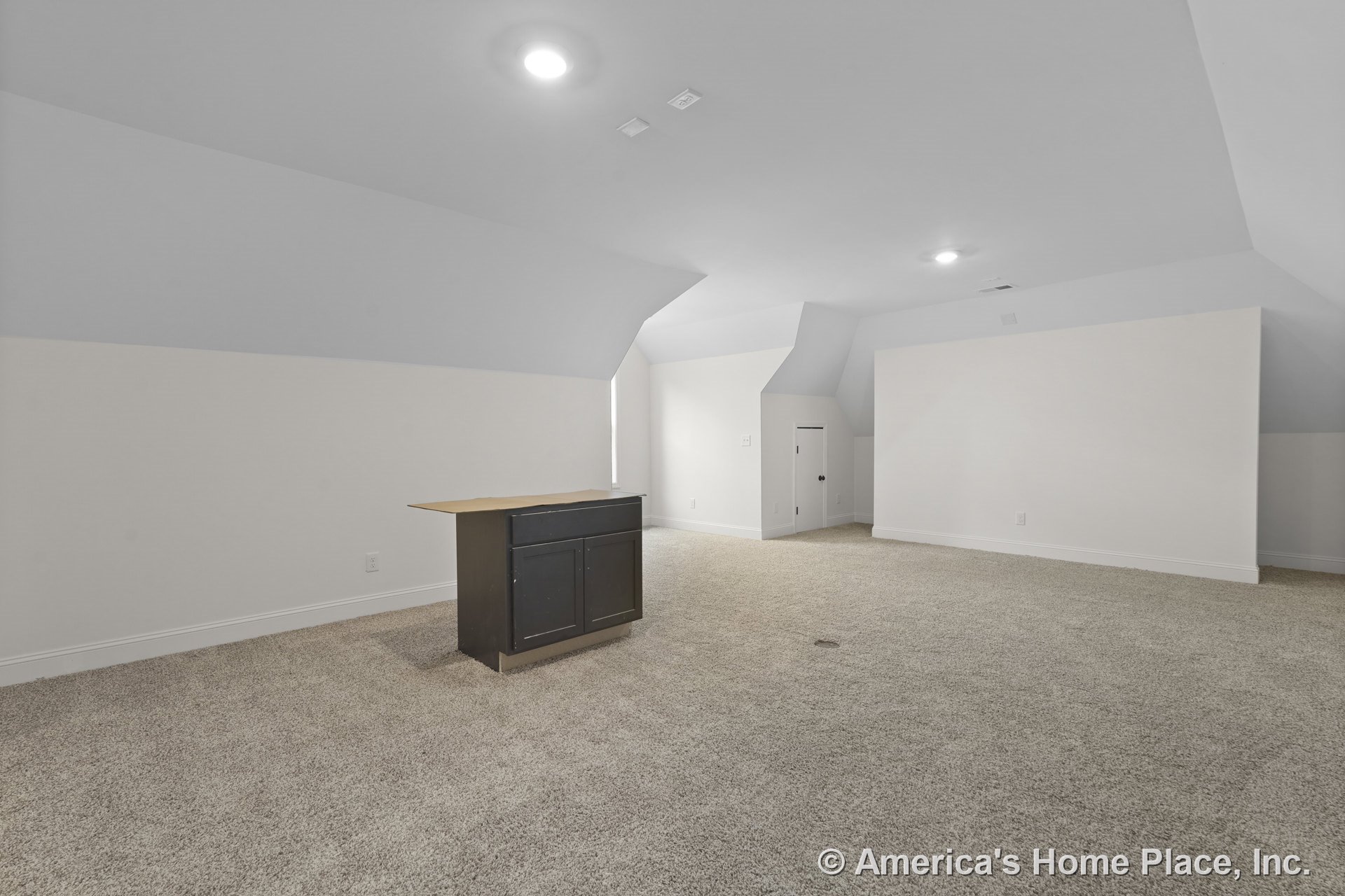 Finished attic bonus room with sloped ceilings, recessed ceiling lights, carpeted floor, dark built-in cabinet, white trim, small access door, and neutral white walls.