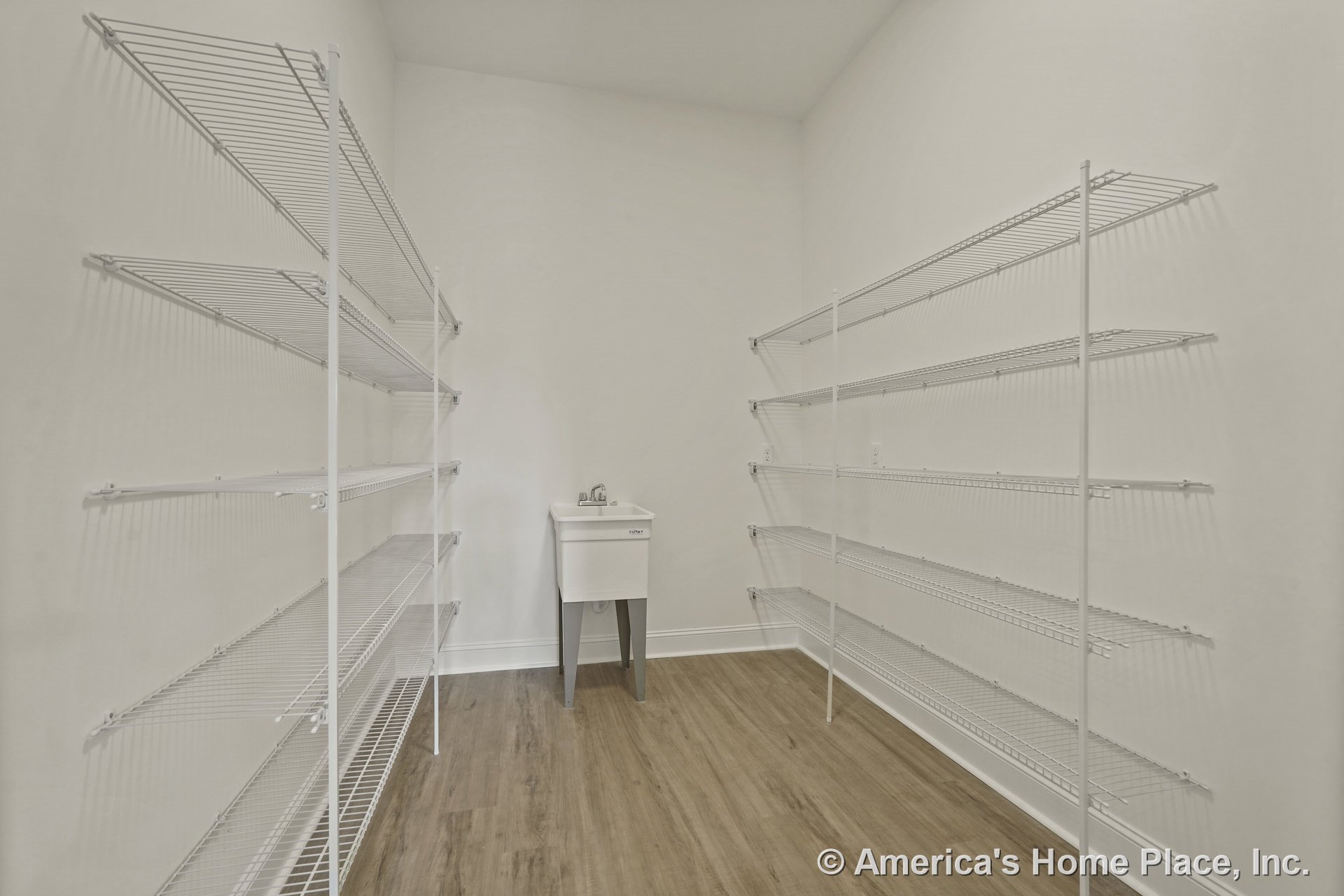 Walk-in pantry with white wire shelving, utility sink, wood-look flooring, high ceiling, white walls, and baseboard trim.