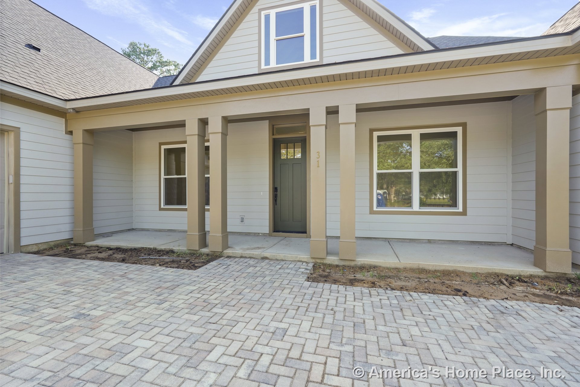Covered front porch with tan square columns, gray paneled front door, double-pane windows, brick paver driveway, and horizontal siding.