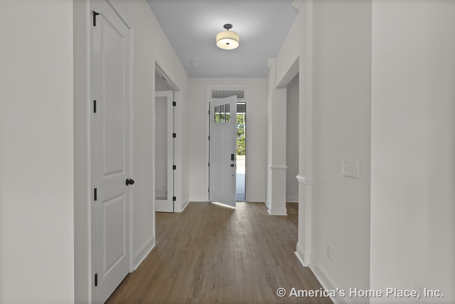 Entry hallway with white paneled doors, wood-look flooring, crown molding trim, transom window above the front door, flush mount ceiling light, baseboards, and open doorway leading
