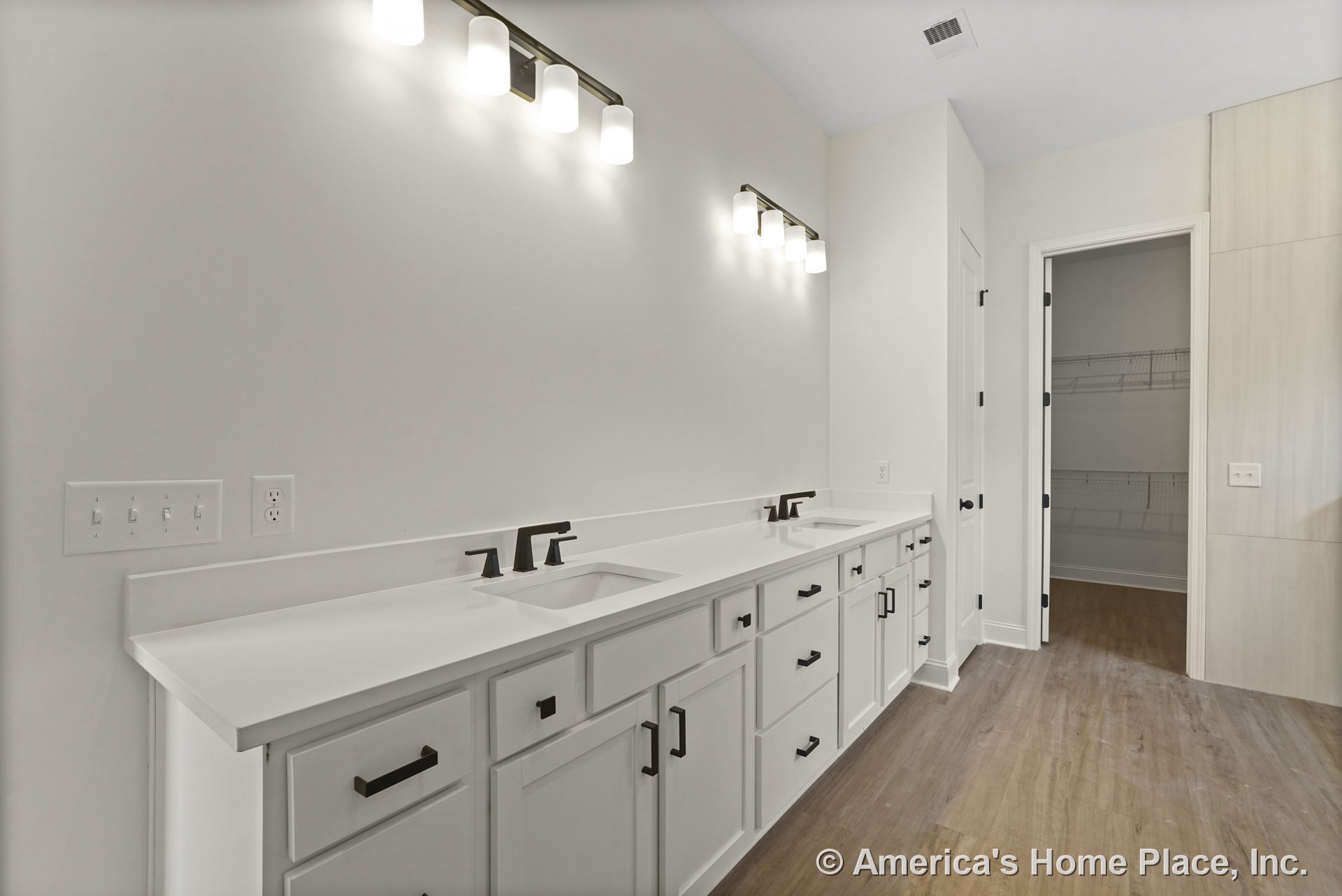 Double vanity with white shaker cabinets, quartz countertop, built-in sinks, black faucet fixtures, wall-mounted modern lights, wood-look flooring, neutral walls, and closet door.