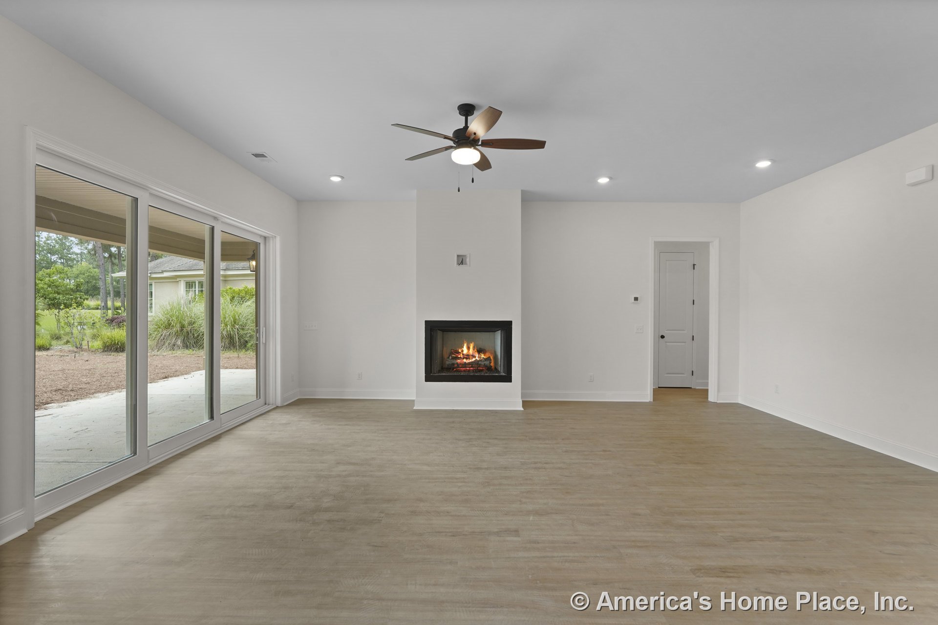 Modern living room with built-in fireplace, wide sliding glass doors, light wood flooring, recessed ceiling lights, ceiling fan with light, white trim, and open layout with neutral