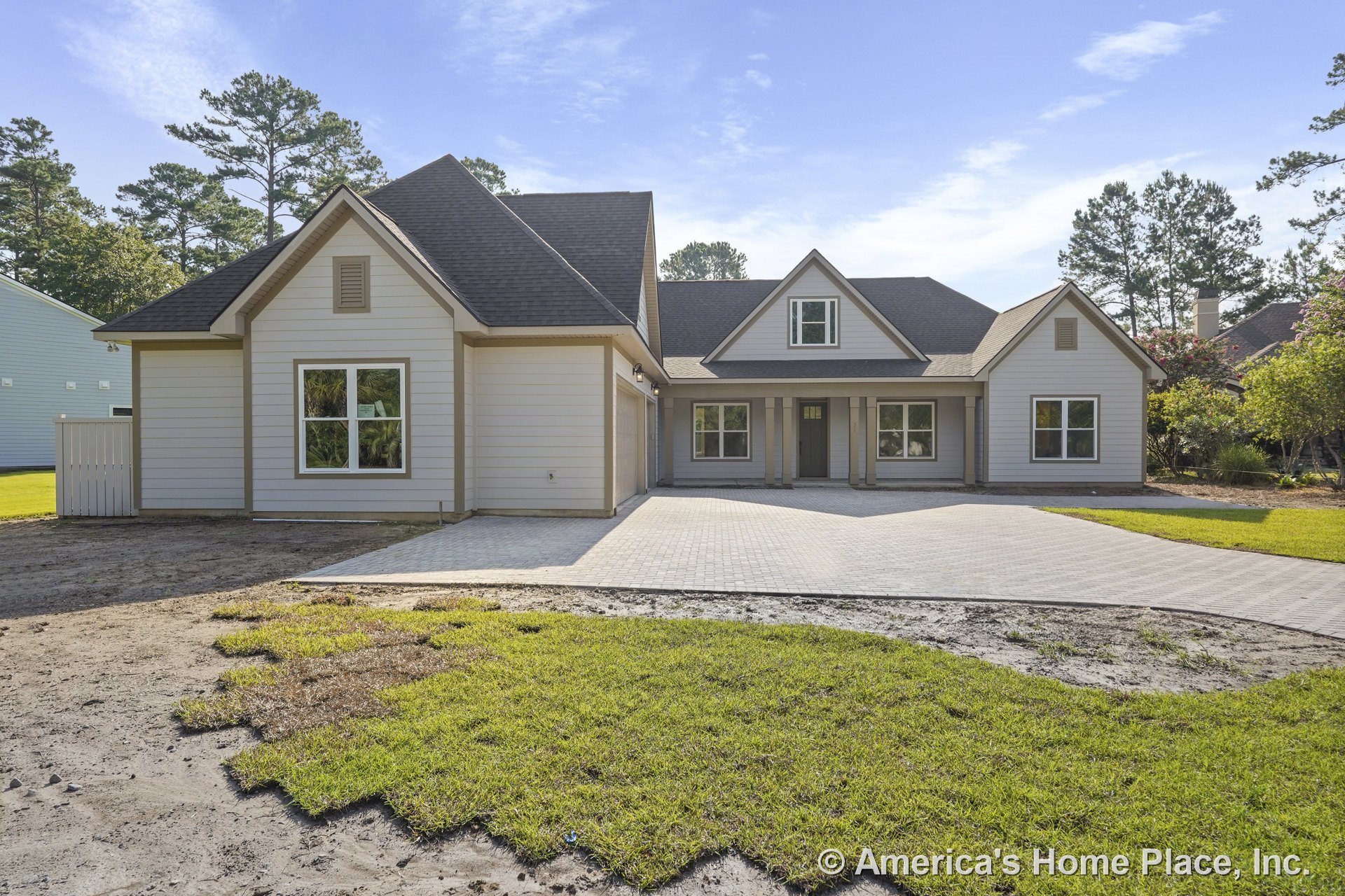 Light-colored exterior with horizontal siding, covered front porch supported by columns, multiple large windows, paved driveway leading to attached garage, gable roof with