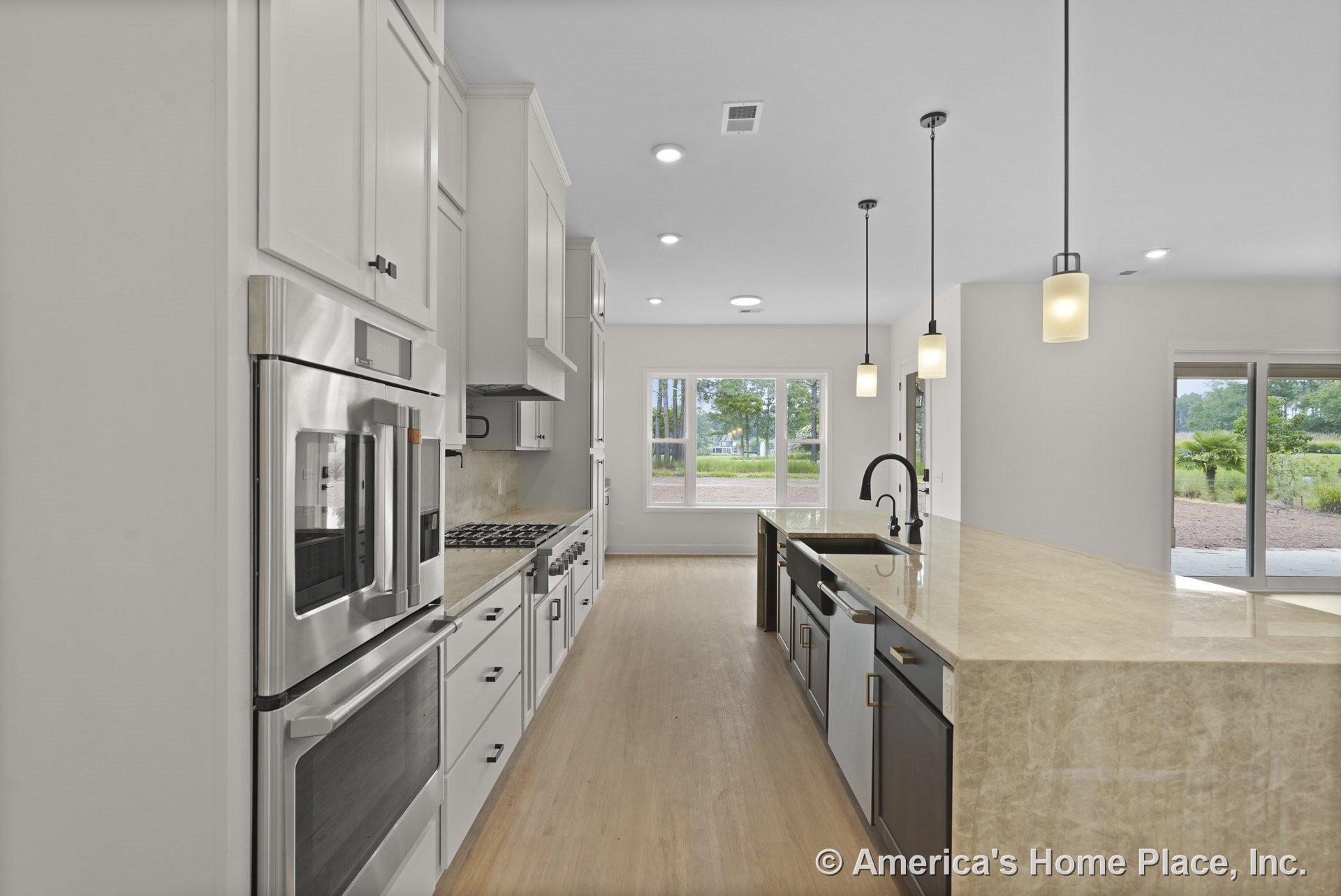 Spacious kitchen with white shaker cabinets, double wall ovens, gas cooktop, marble countertops, large marble island with undermount sink, pendant lighting, wood flooring, and