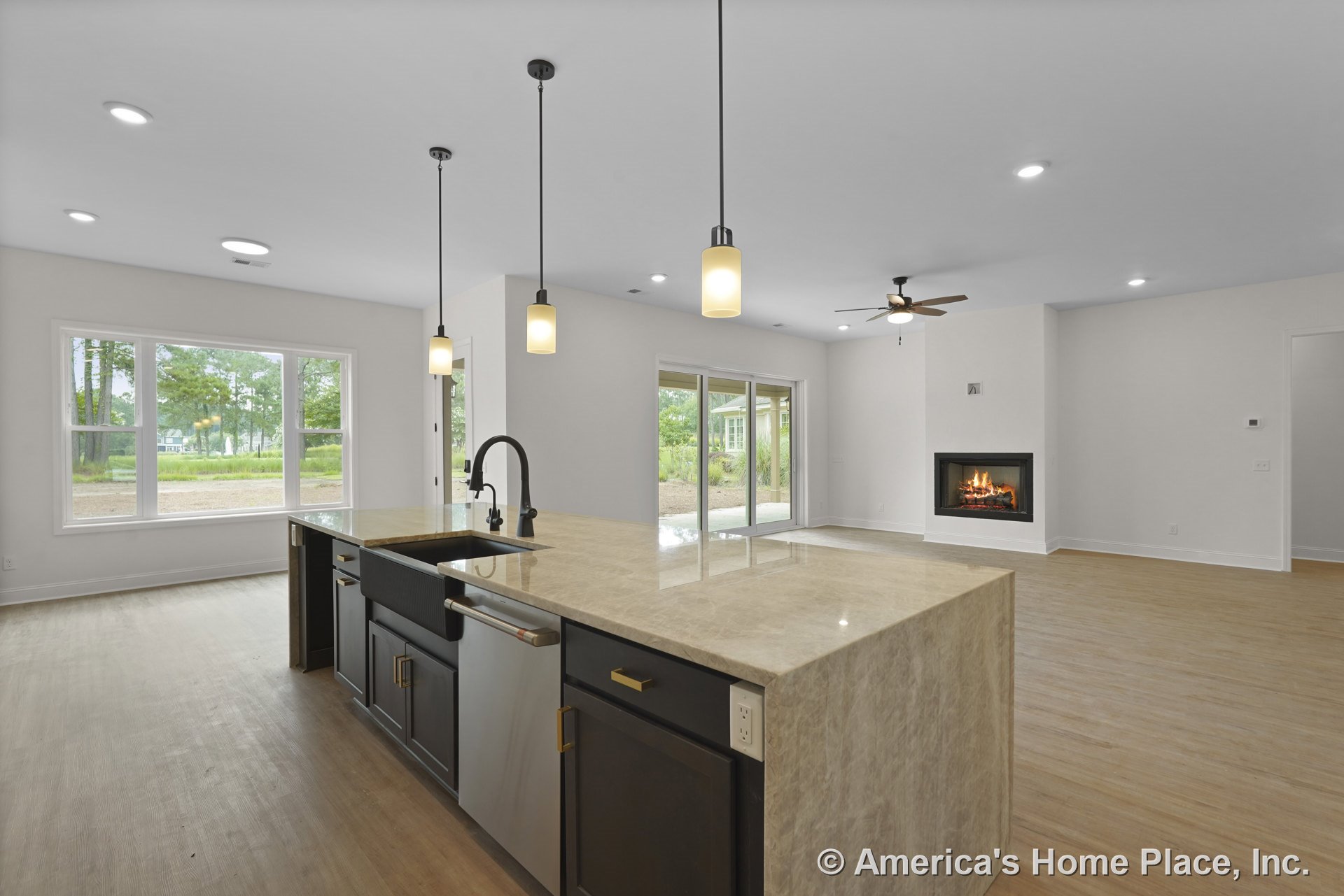 Open kitchen with a large stone island featuring a built-in sink, black cabinetry, pendant lighting, and wood flooring; adjacent living area includes a modern fireplace, ceiling
