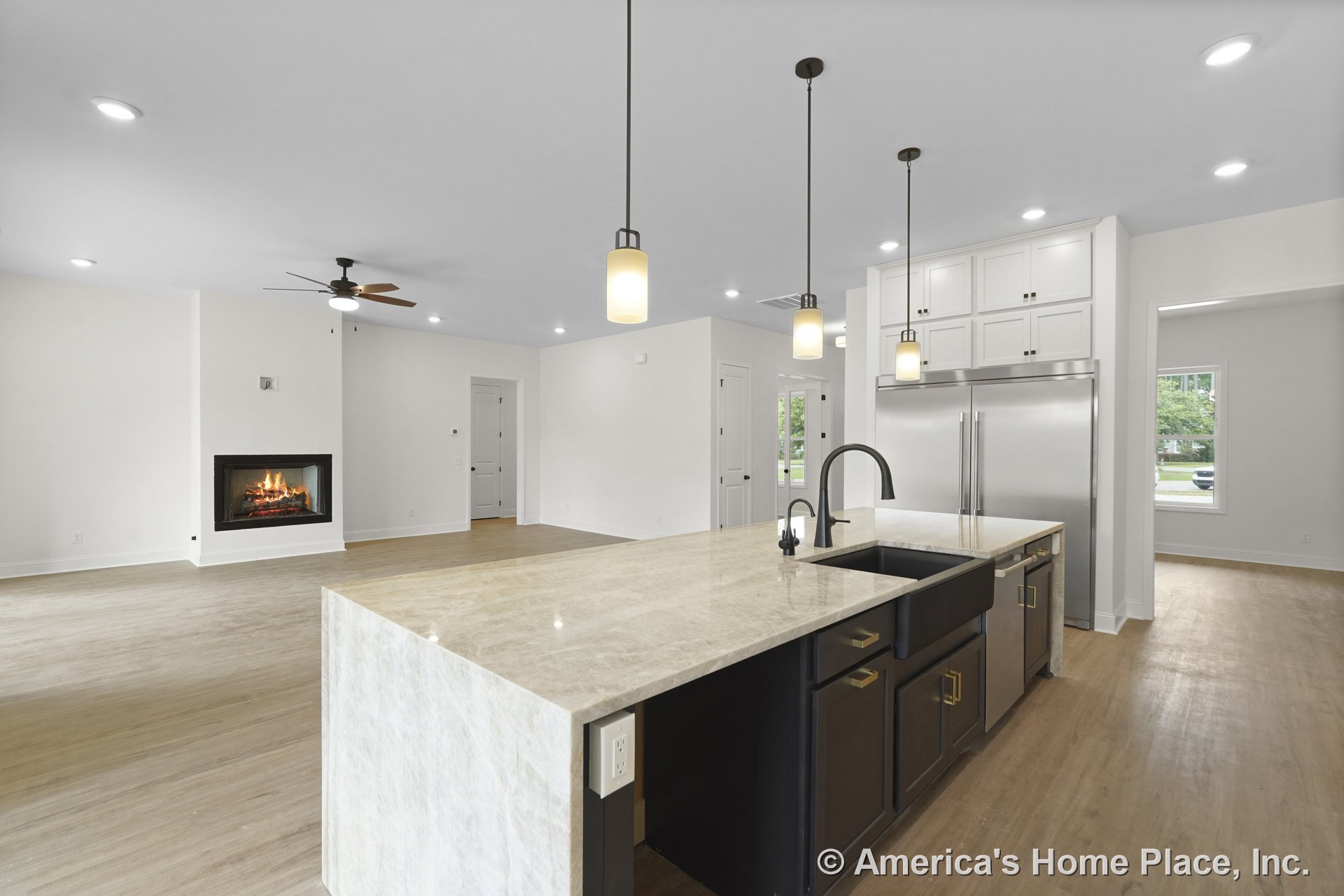 Marble kitchen island with black undermount sink and pendant lights, surrounded by white upper cabinetry and built-in stainless refrigerator; open floor plan connects to living