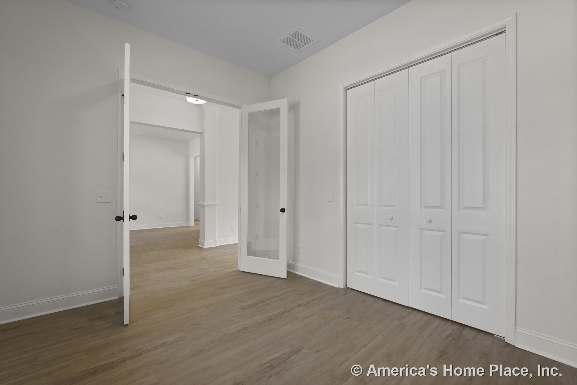 Double glass doors, large closet with paneled doors, wood-look flooring, white walls, baseboards, recessed ceiling vent, flush mount ceiling light, and white trim.