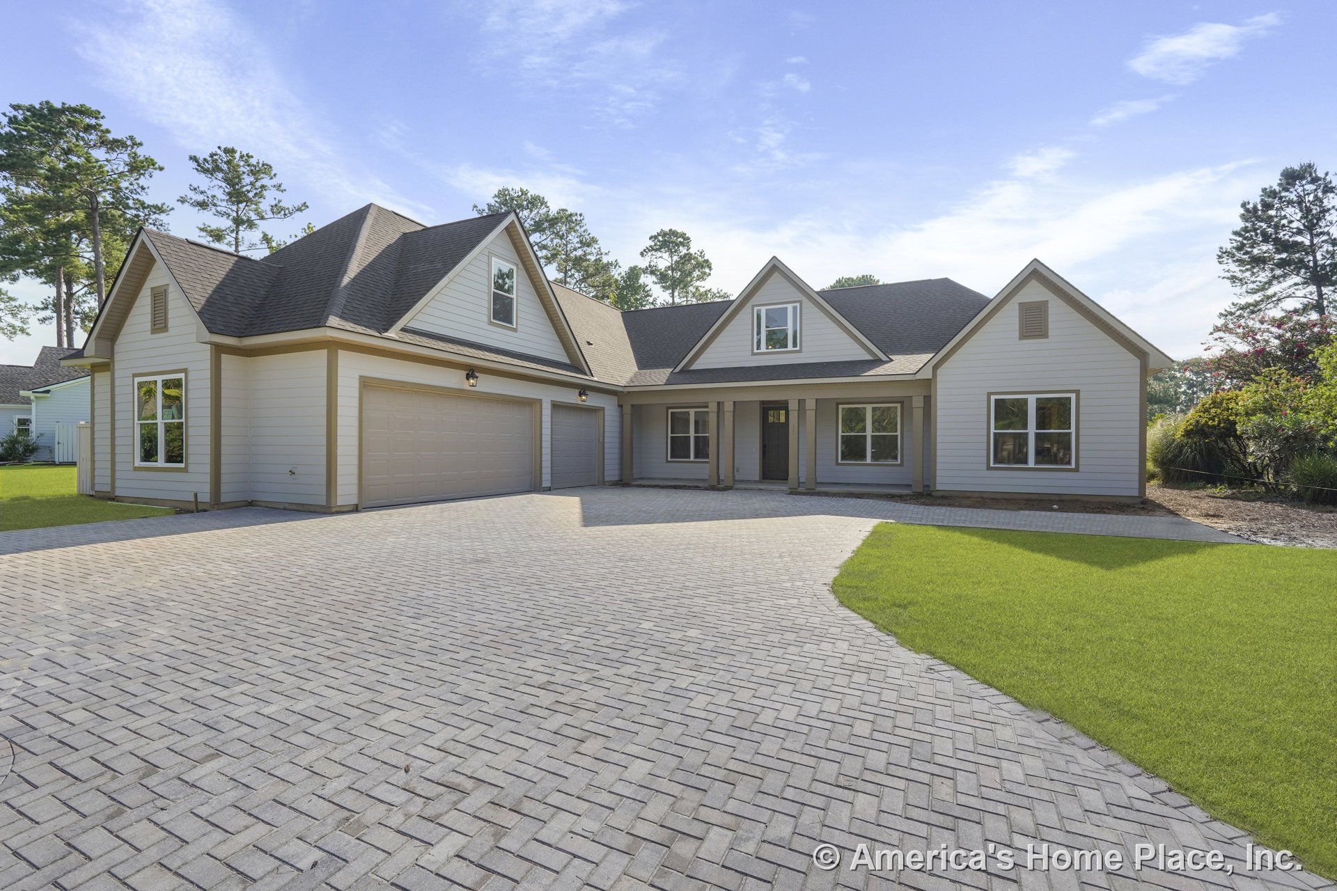 Light-colored horizontal lap siding, three-car garage with paneled doors, covered front porch, double-hung windows, paved herringbone driveway, gable roof, exterior trim, and