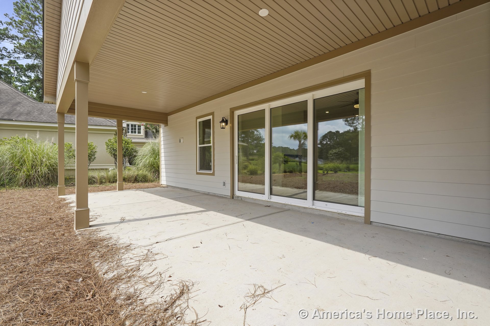 Covered patio with beige paneled ceiling, concrete floor, exterior wall siding, double sliding glass doors, single trimmed window, outdoor wall sconce, and structural columns.