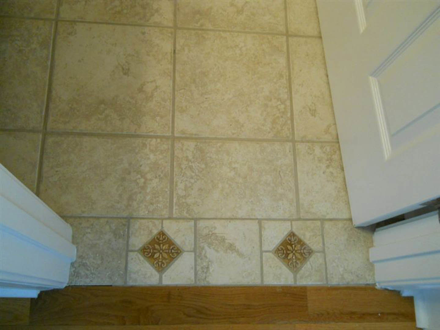 Beige tile flooring leading to a white paneled door, adjacent to a smooth white plaster wall