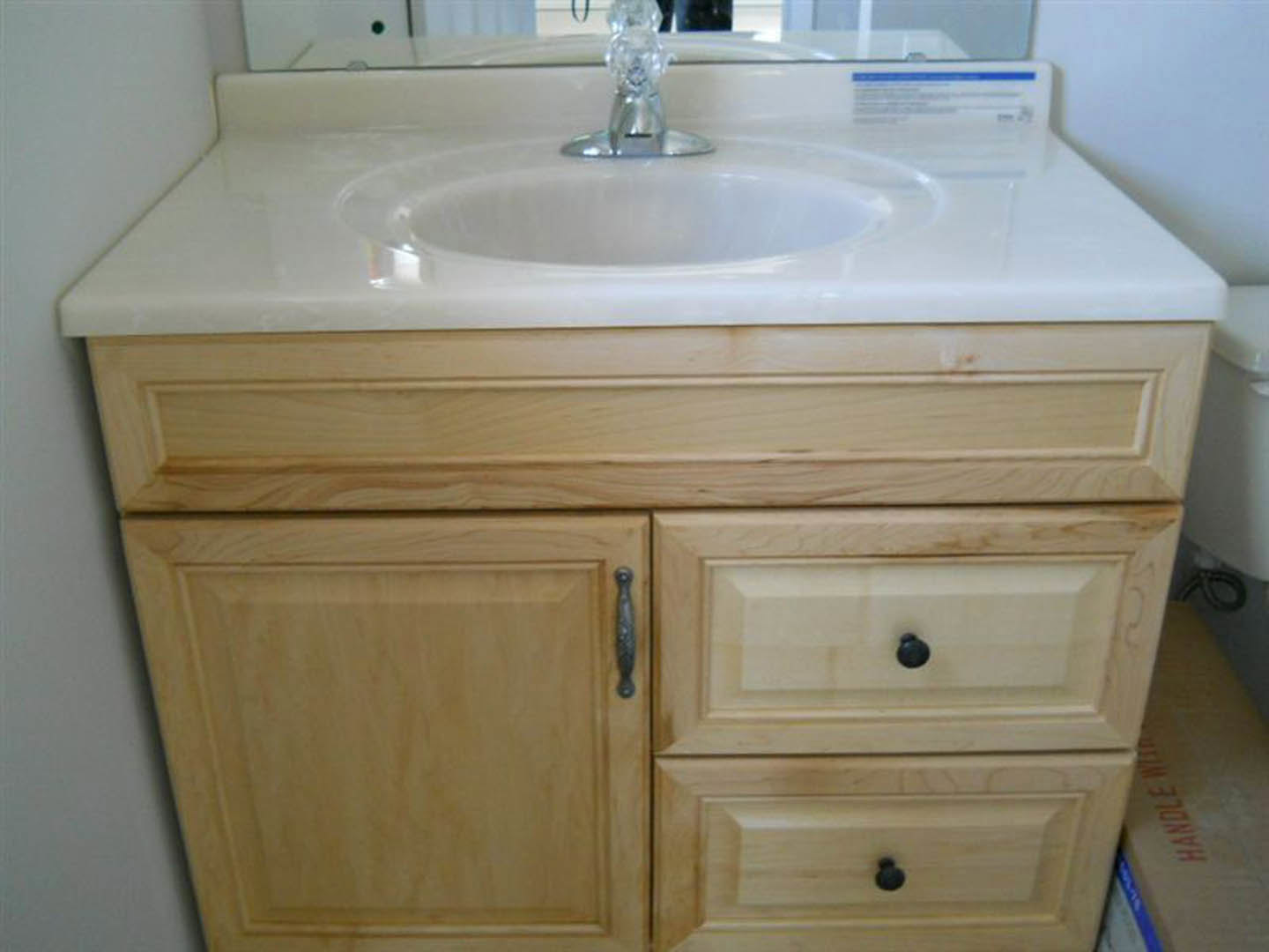 White ceramic sink with chrome faucet set in a light wood vanity, rectangular mirror mounted above, neutral wall and countertop visible