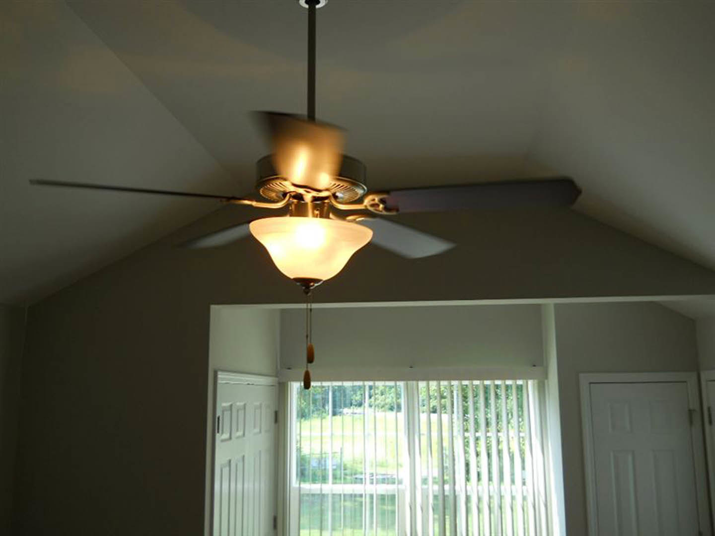Ceiling fan with brushed metal finish mounted on white ceiling, window with horizontal blinds, white paneled door, recessed lighting fixtures, neutral painted walls